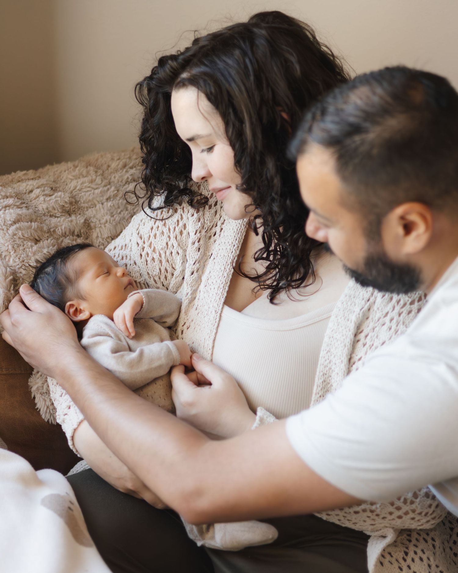 Parents cradling their newborn baby on a cozy blanket.
