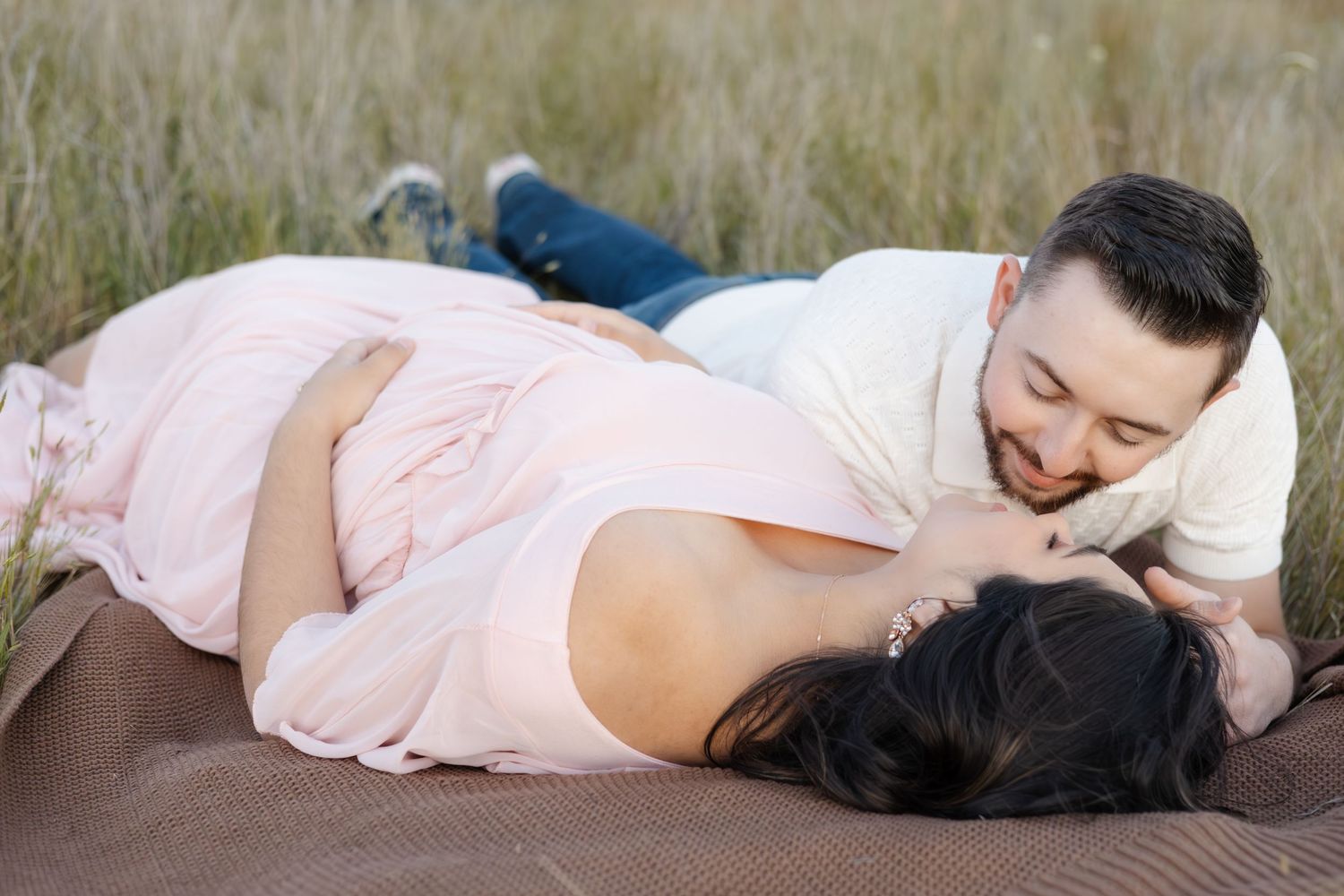 Romantic outdoor photoshoot with couple lying on blanket in natural setting.