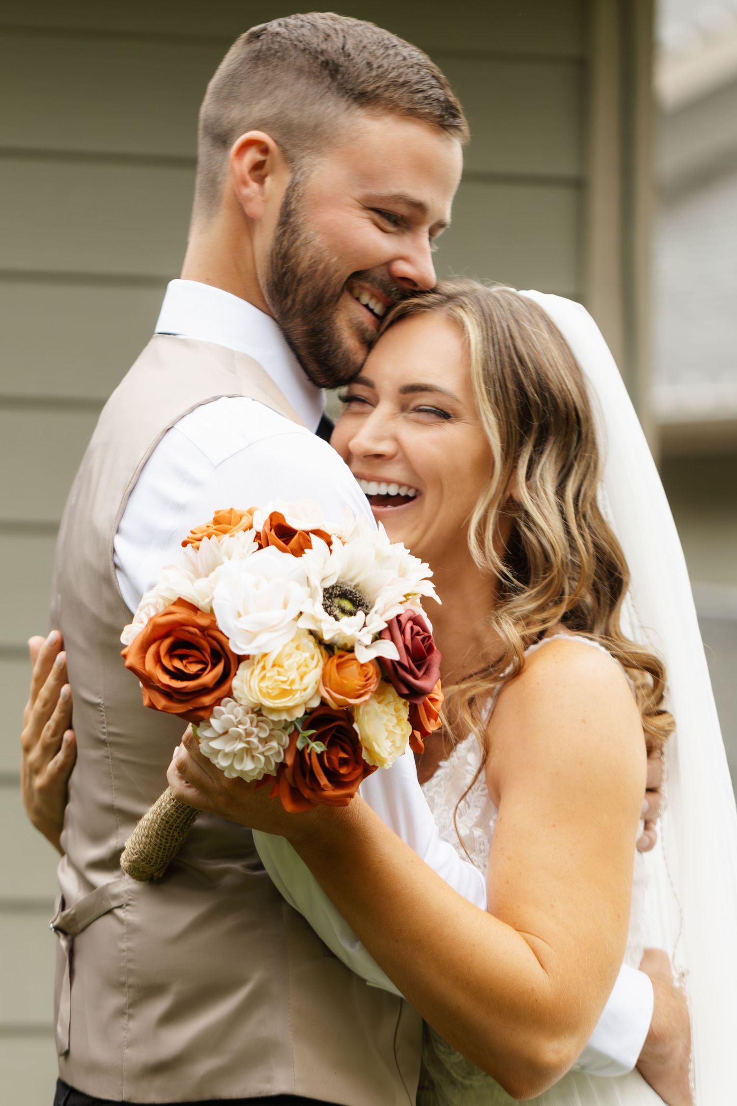 A couple shares an intimate moment with autumn-colored roses in their wedding attire.
