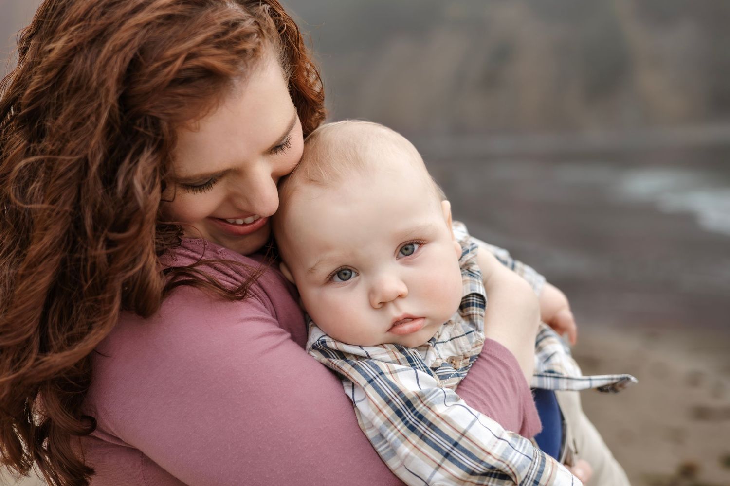 A tender moment captured between parent and baby against a moody outdoor backdrop.