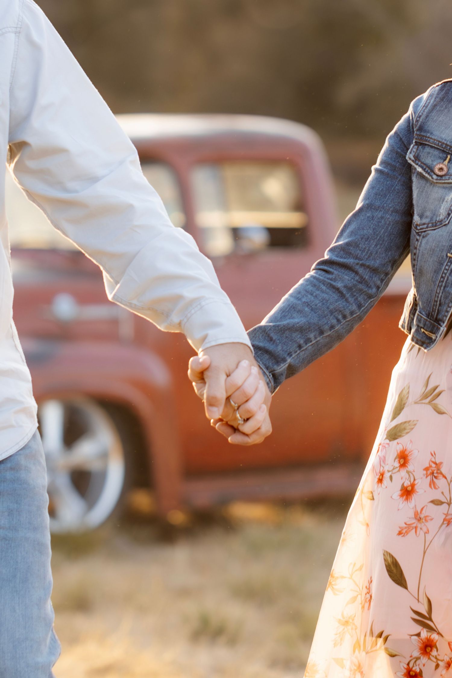 Close-up of people holding hands while walking, with a red vintage truck visible in background.