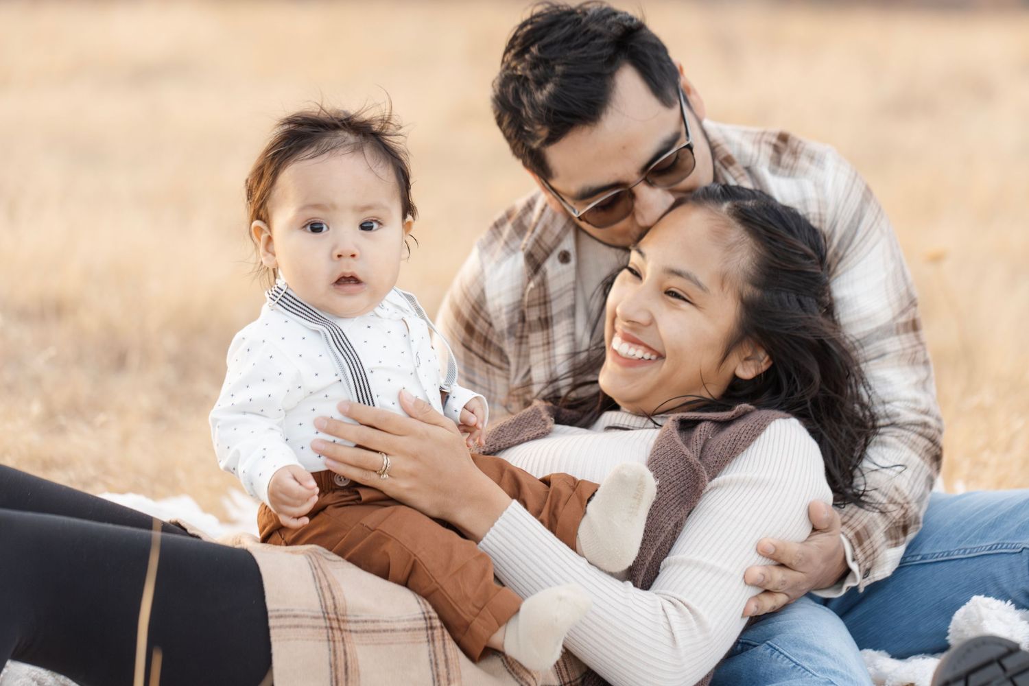 Happy family moment captured while relaxing on picnic blanket in autumn field.