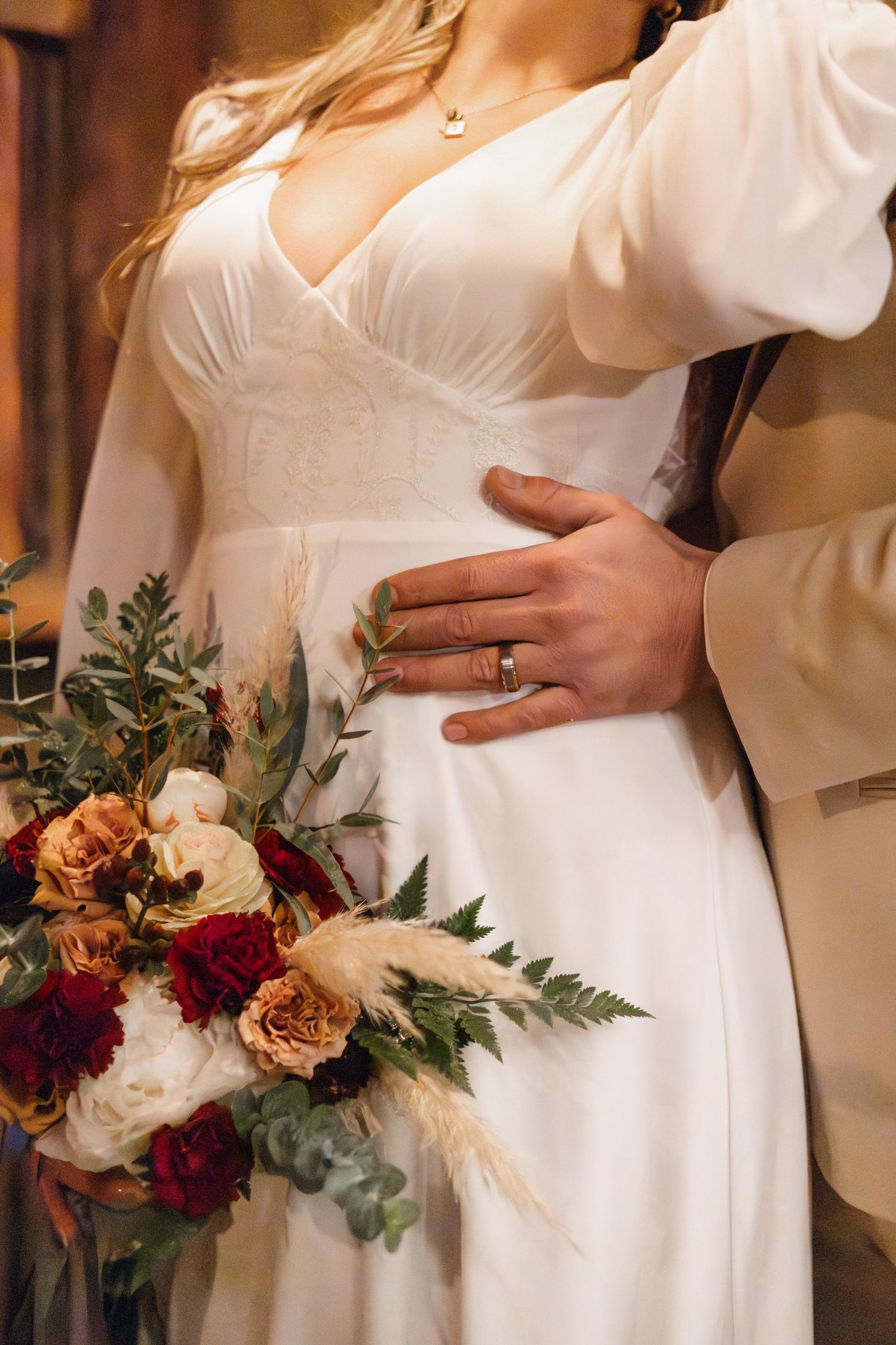 Close-up of bride's white dress with lace details and burgundy floral bouquet.