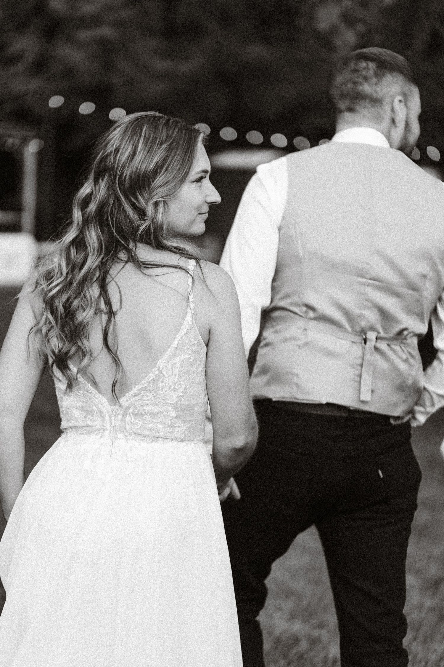A black and white wedding photo showing a bride in a lace gown standing beside a groom wearing a vest.
