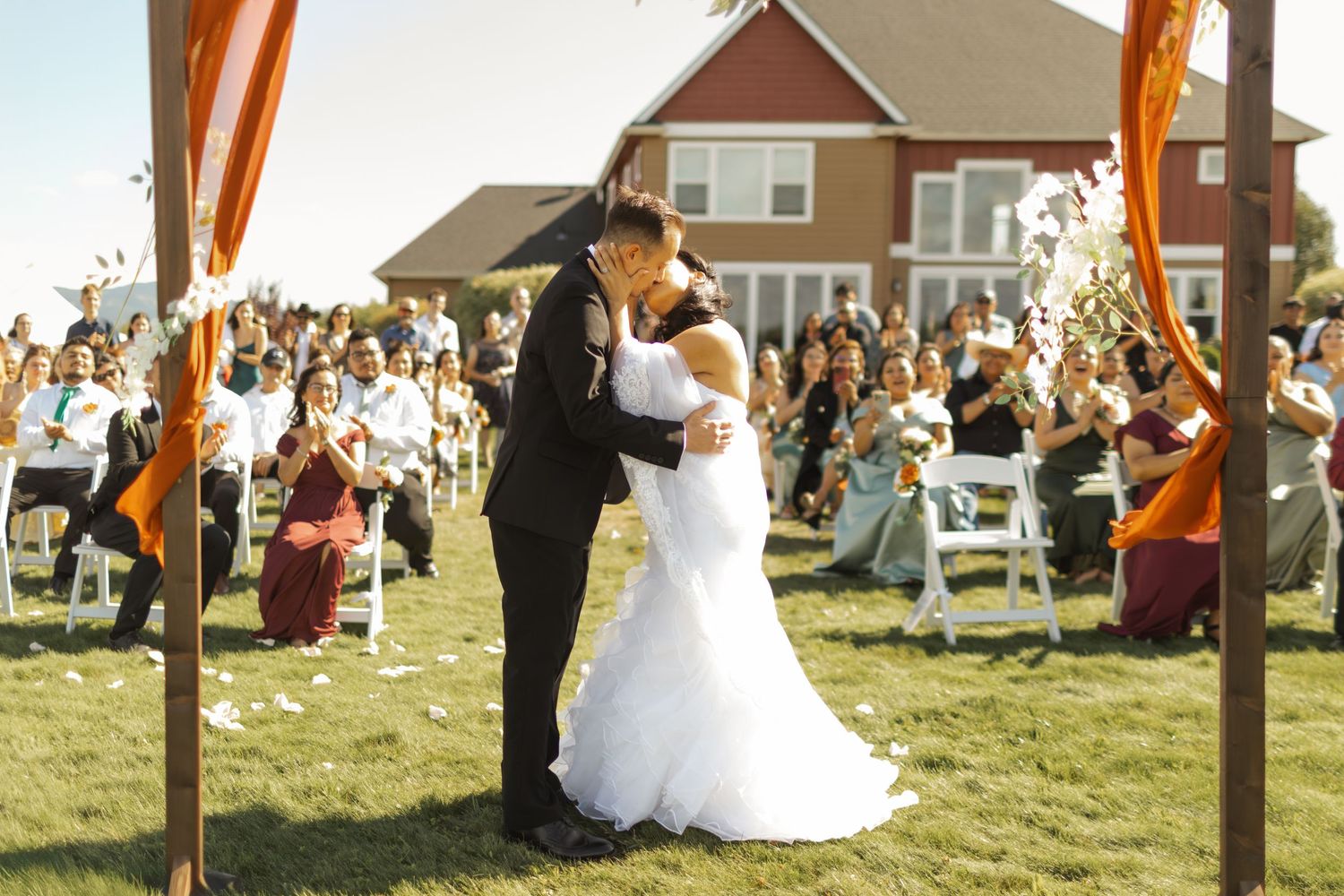 Wedding ceremony setup outdoors with white chairs and decorative poles on a sunny lawn.