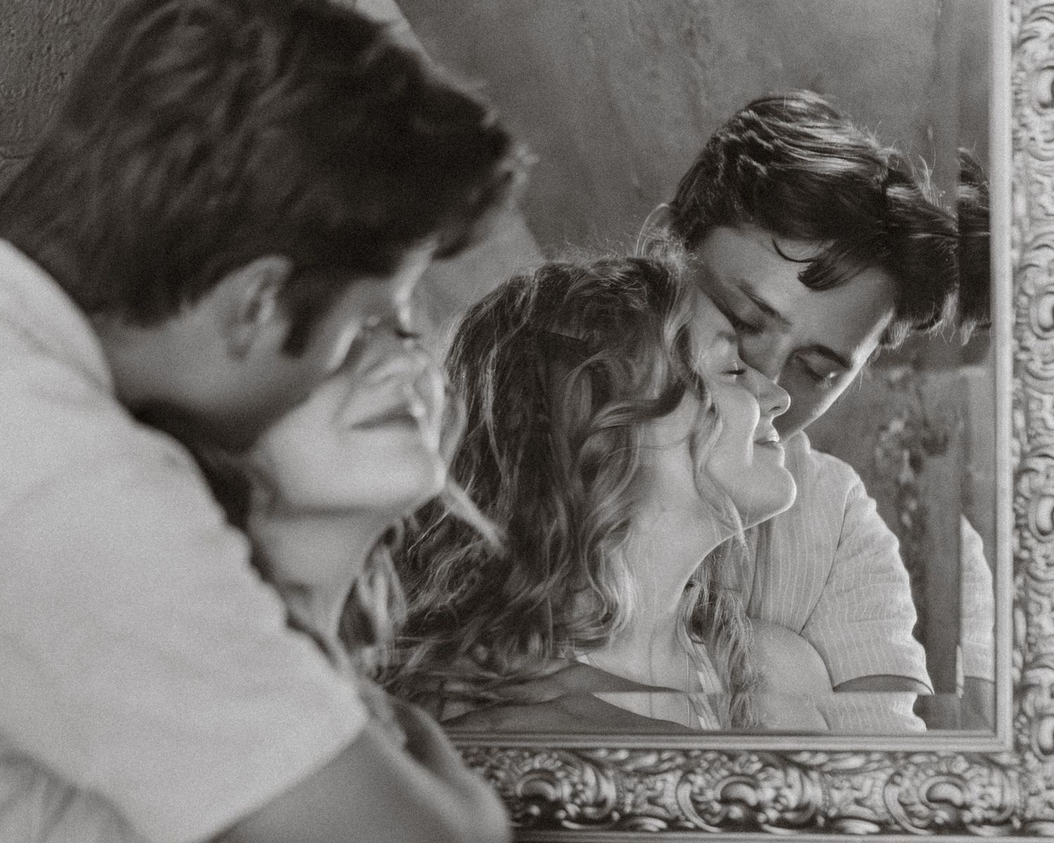 Black and white photo of a romantic couple sharing an intimate moment reflected in an ornate vintage mirror.