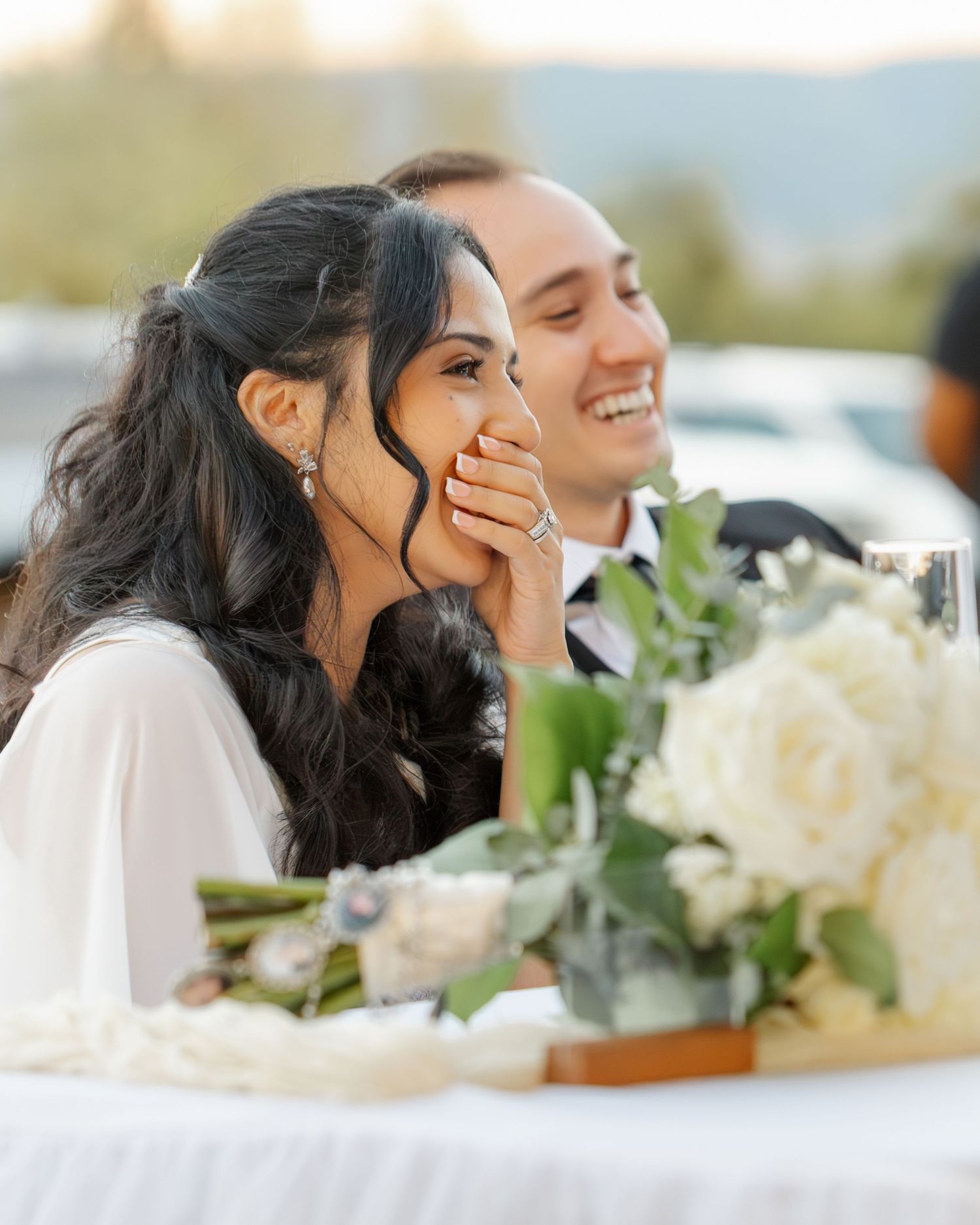 A joyful wedding reception scene with white floral centerpieces on an outdoor table.
