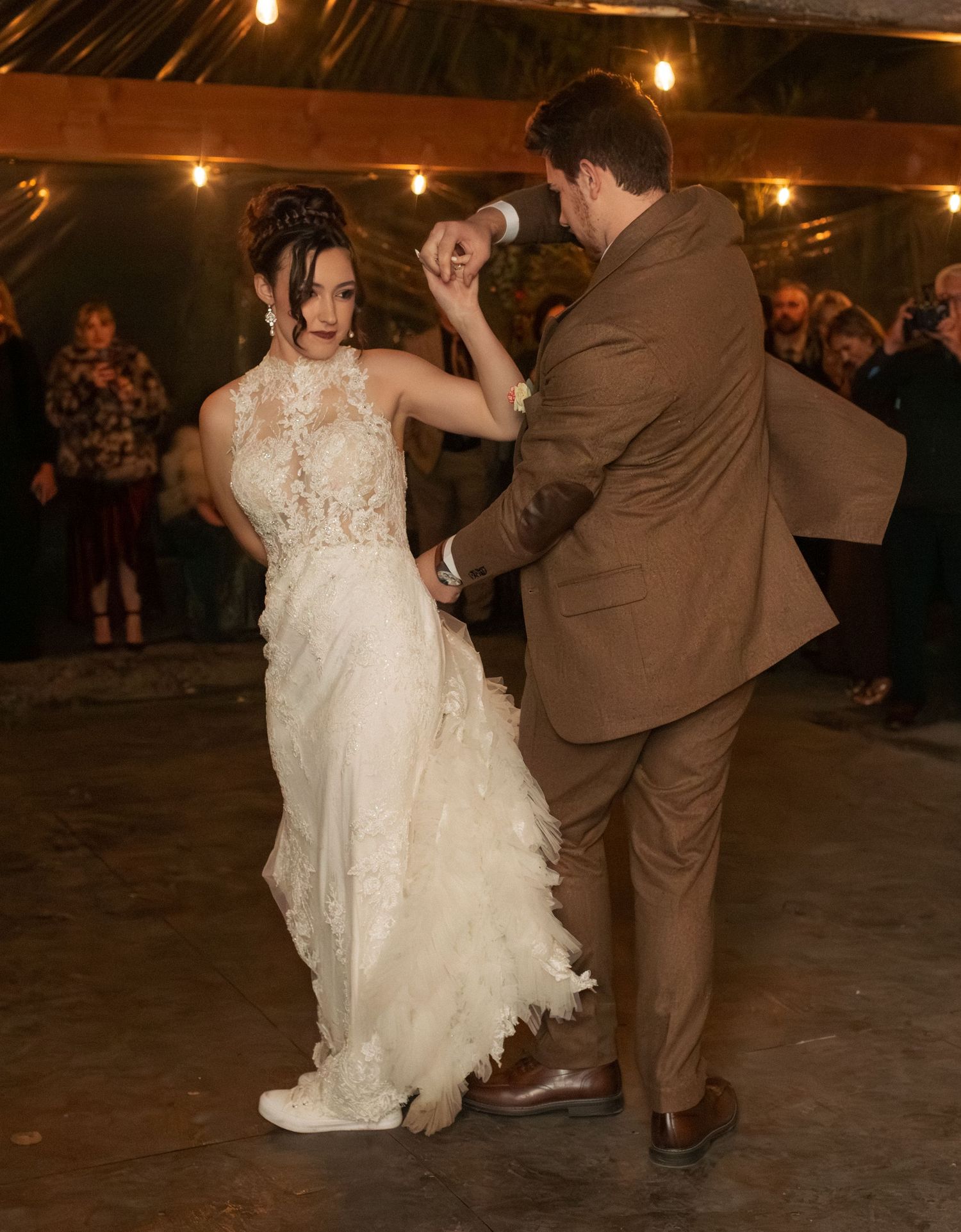 Wedding couple performs playful dance move on rustic venue floor during reception.