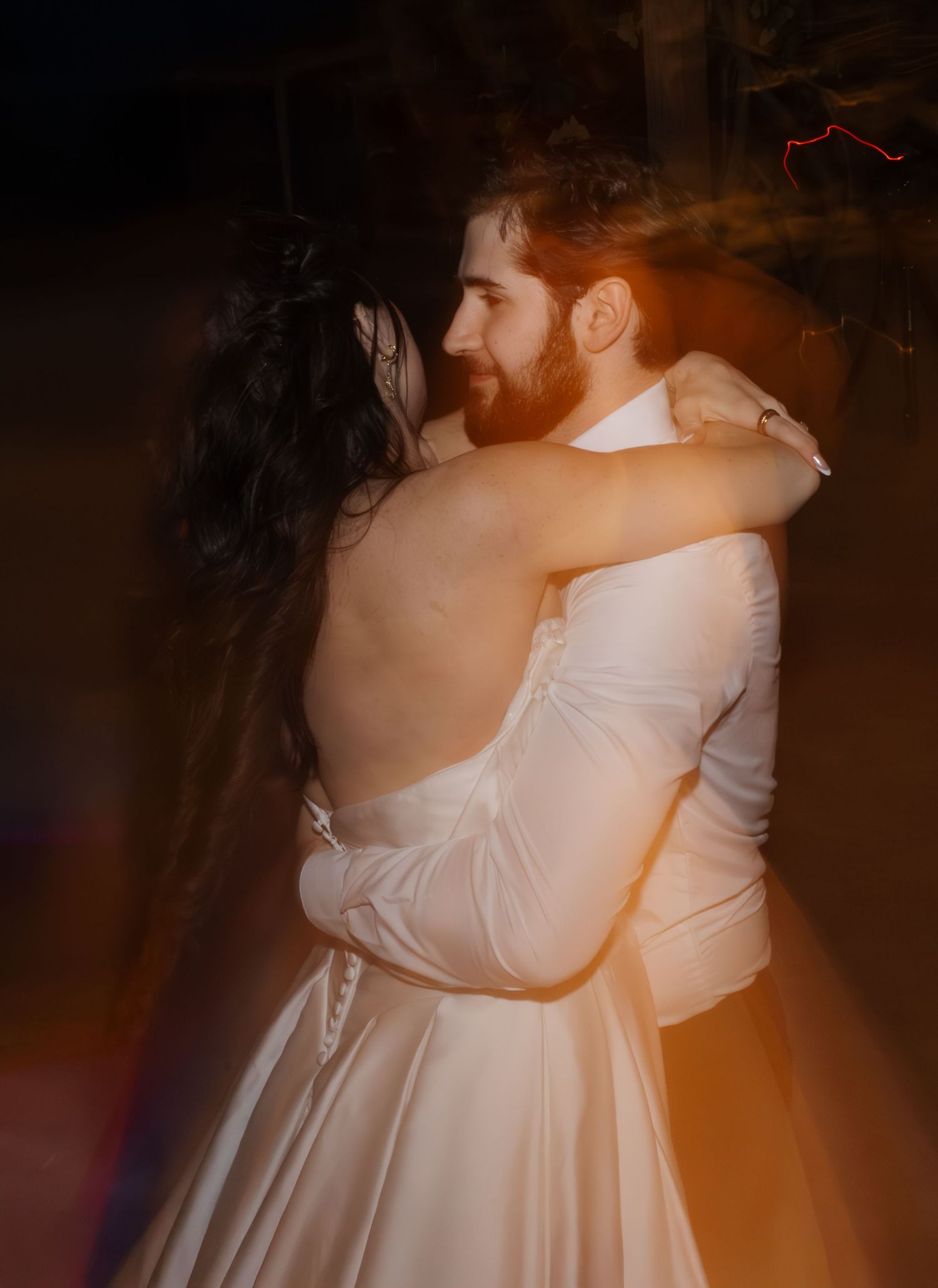 A couple in wedding attire shares a romantic dance together in a dimly lit room with warm lighting.