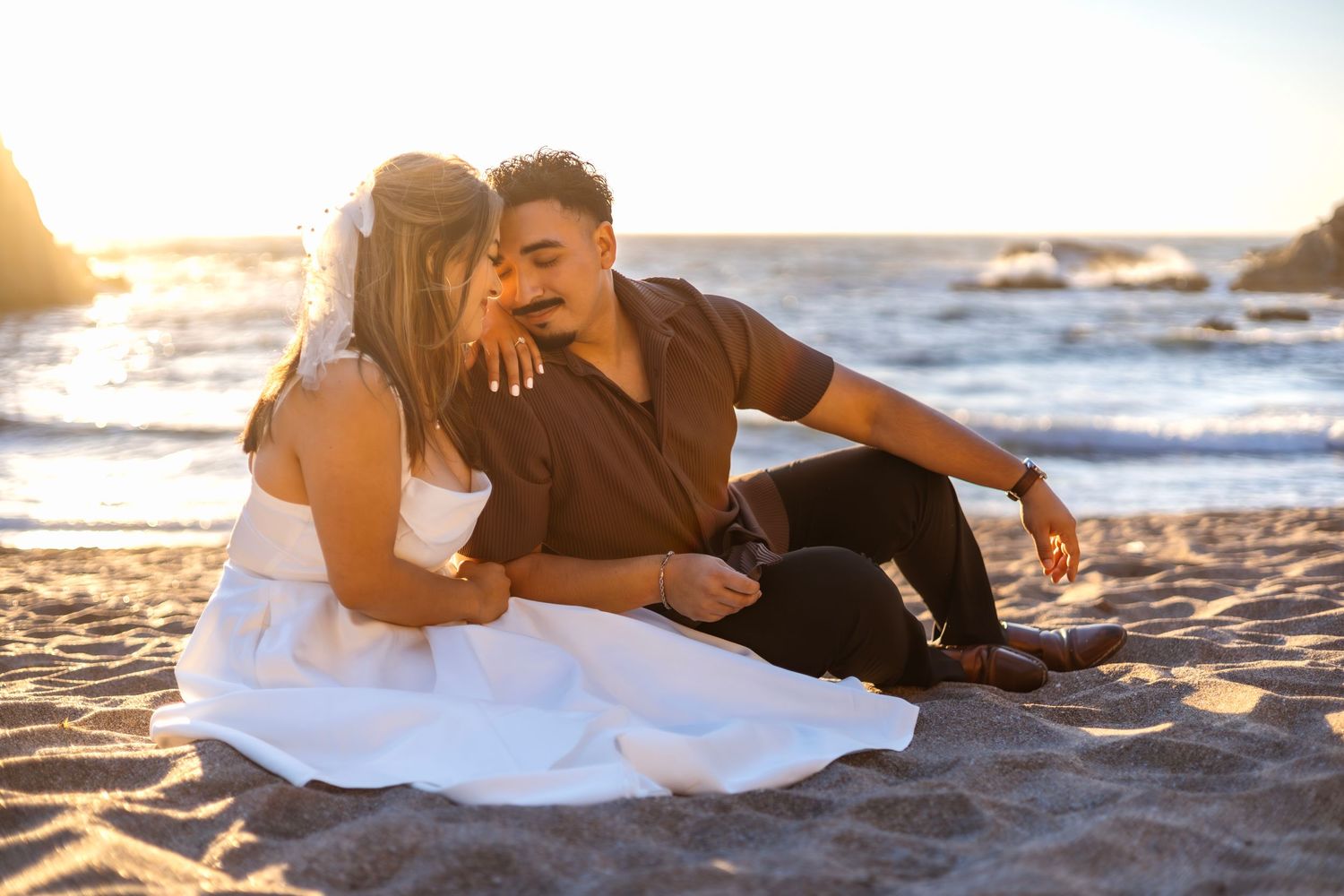 Couple lying on beach sand during golden hour sunset photography session.