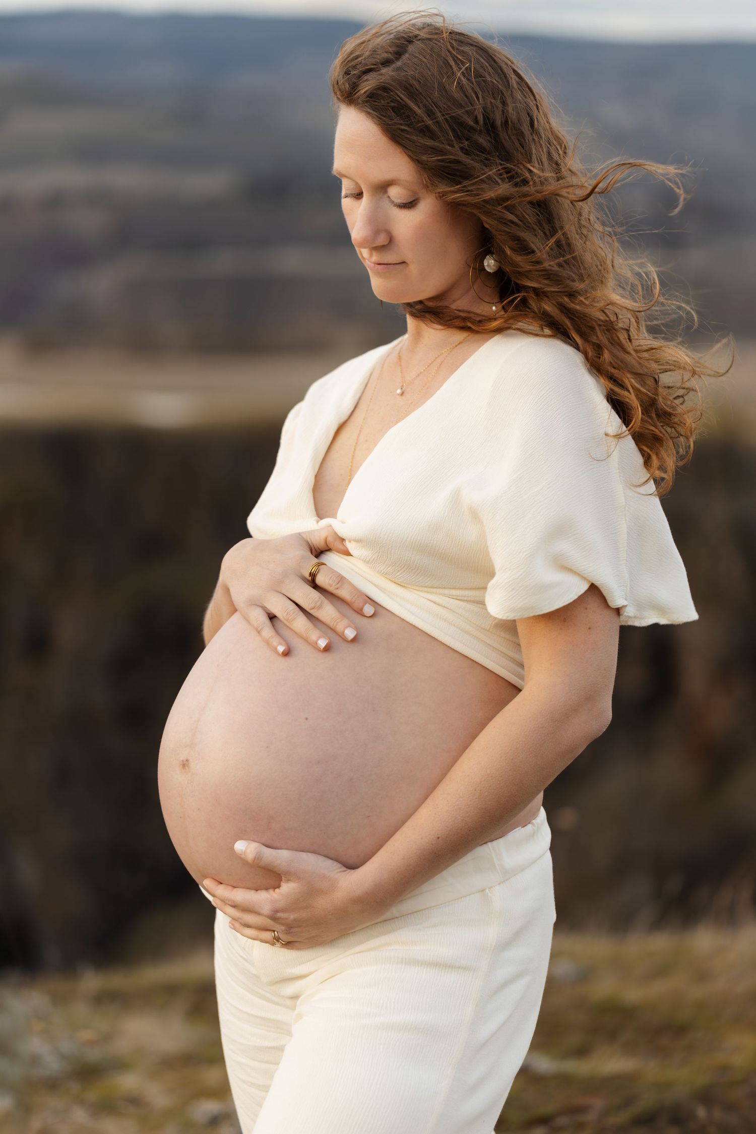 Serene maternity portrait against mountain backdrop with flowing white dress.