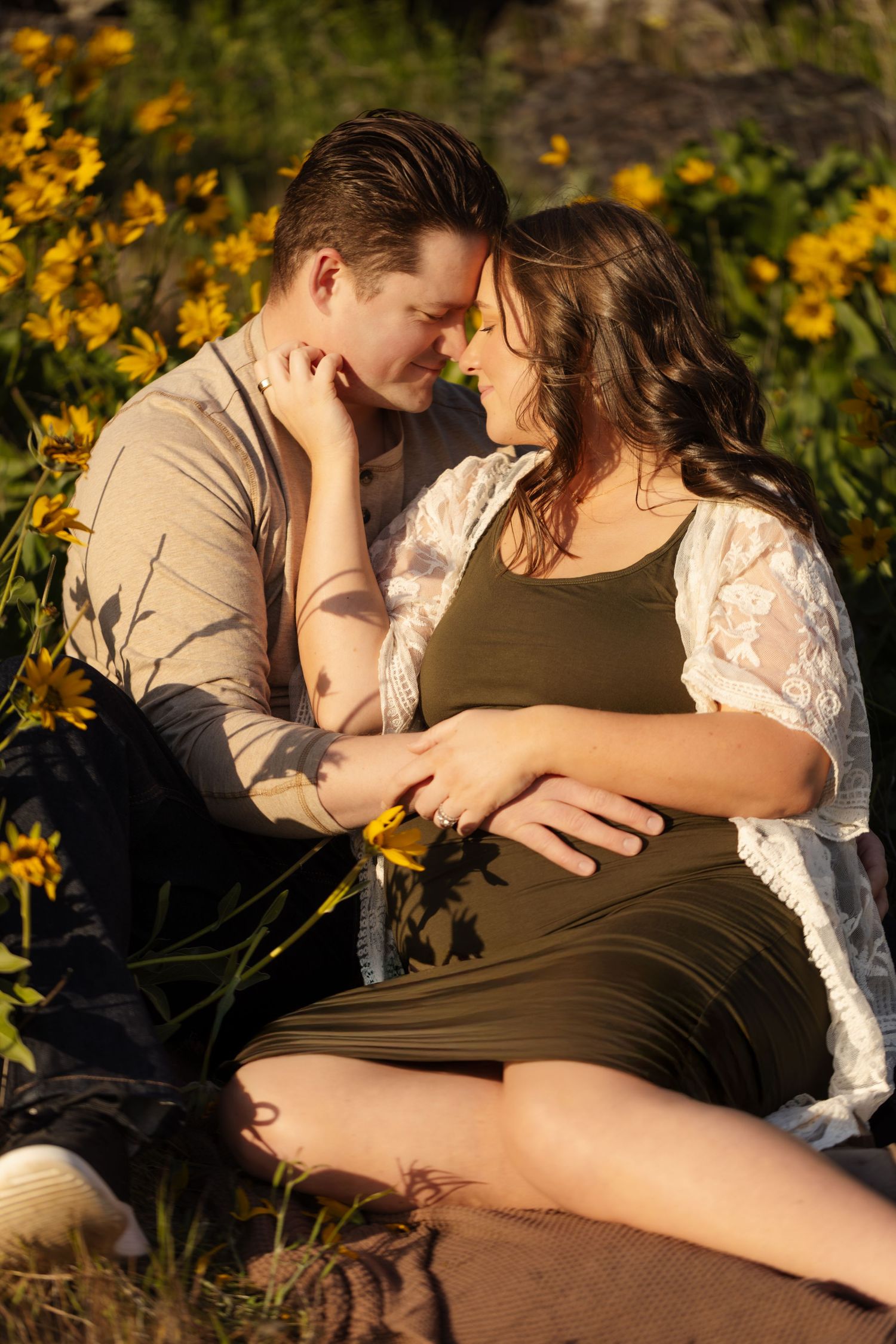 Romantic couple embraces among yellow wildflowers during sunset maternity photoshoot.