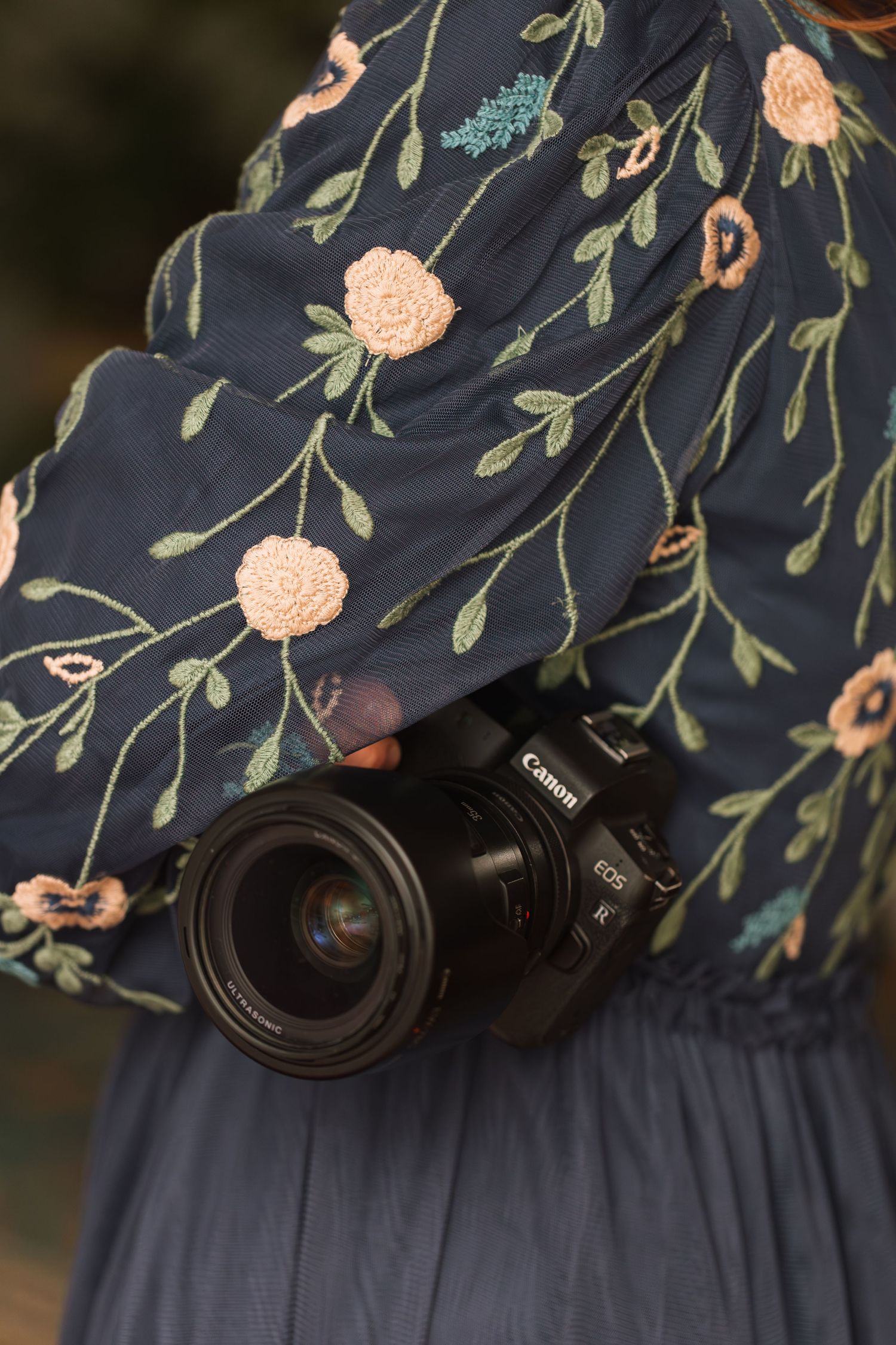 A Canon camera lens against a navy blue floral patterned fabric background.