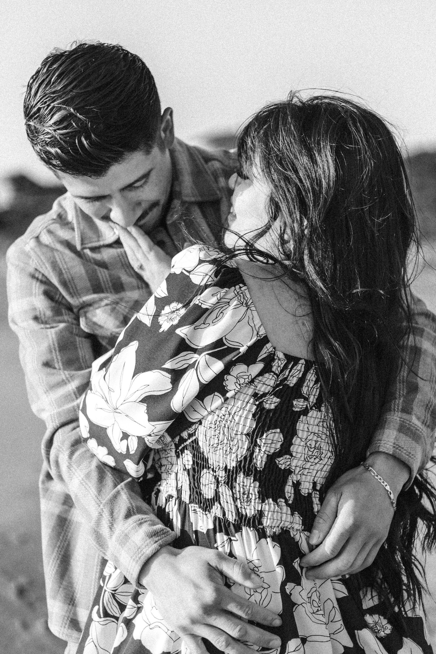 Couple in black and white sharing intimate embrace wearing floral dress and plaid shirt.