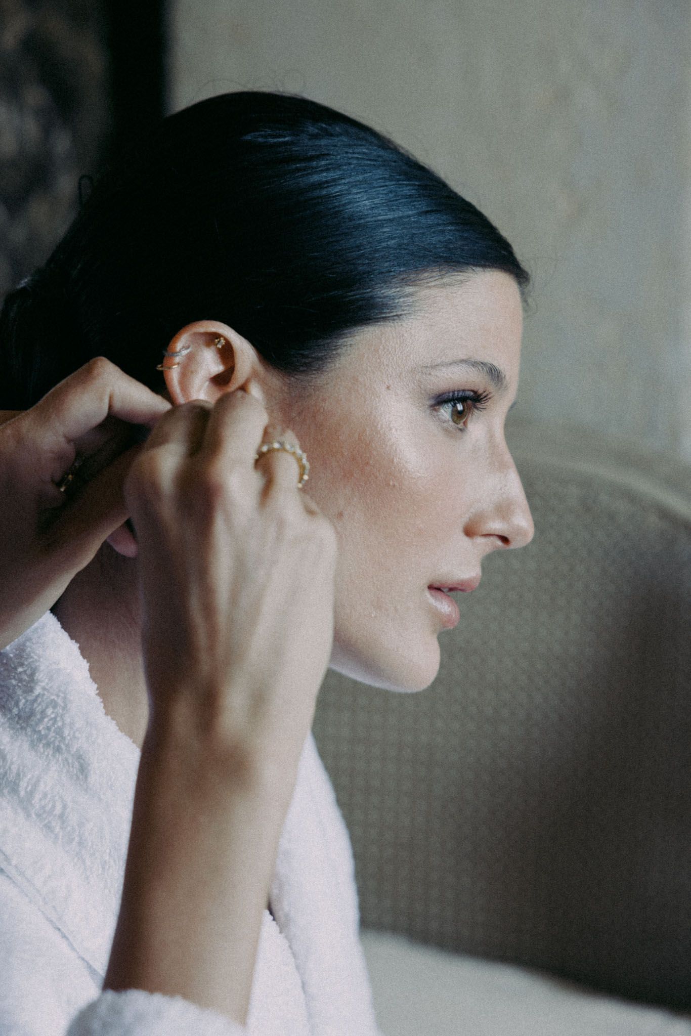 Side profile of someone putting on earrings while wearing a soft pink robe.