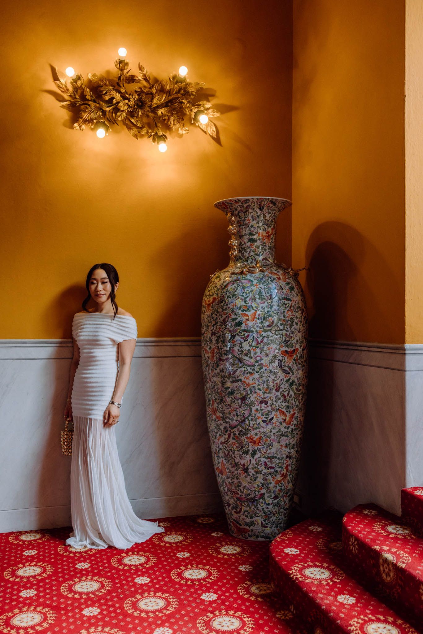 Wedding dress photographed against orange walls with decorative vase and red patterned carpet.