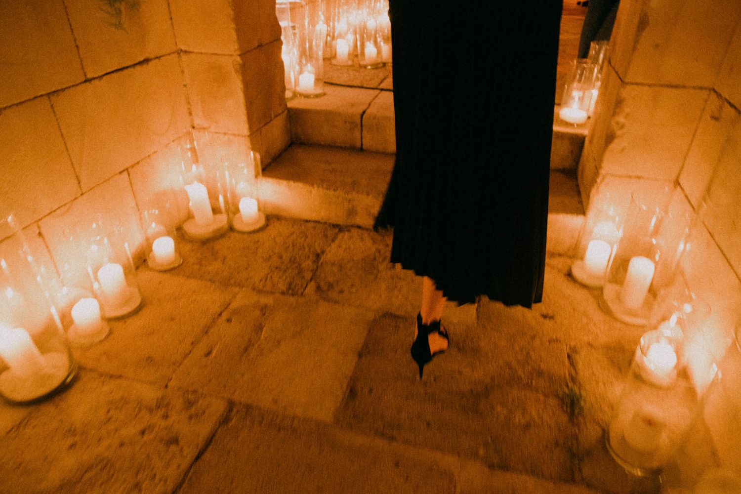 White pillar candles arranged in a circle on a stone floor create a warm, glowing atmosphere in dim lighting.