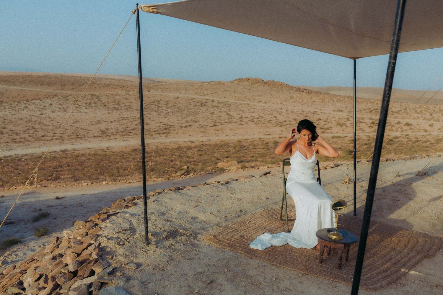 Desert campsite with beige shade canopy set up in arid landscape during golden hour.