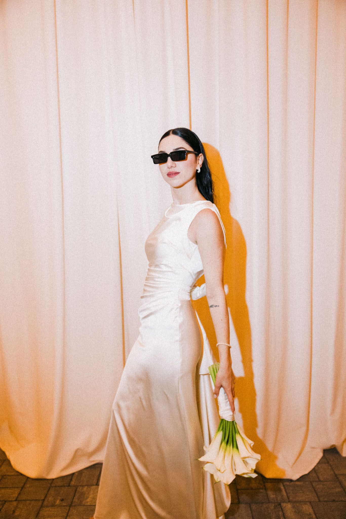 A bride in a white wedding gown poses against a peach-colored curtain backdrop in a series of artistic shots.