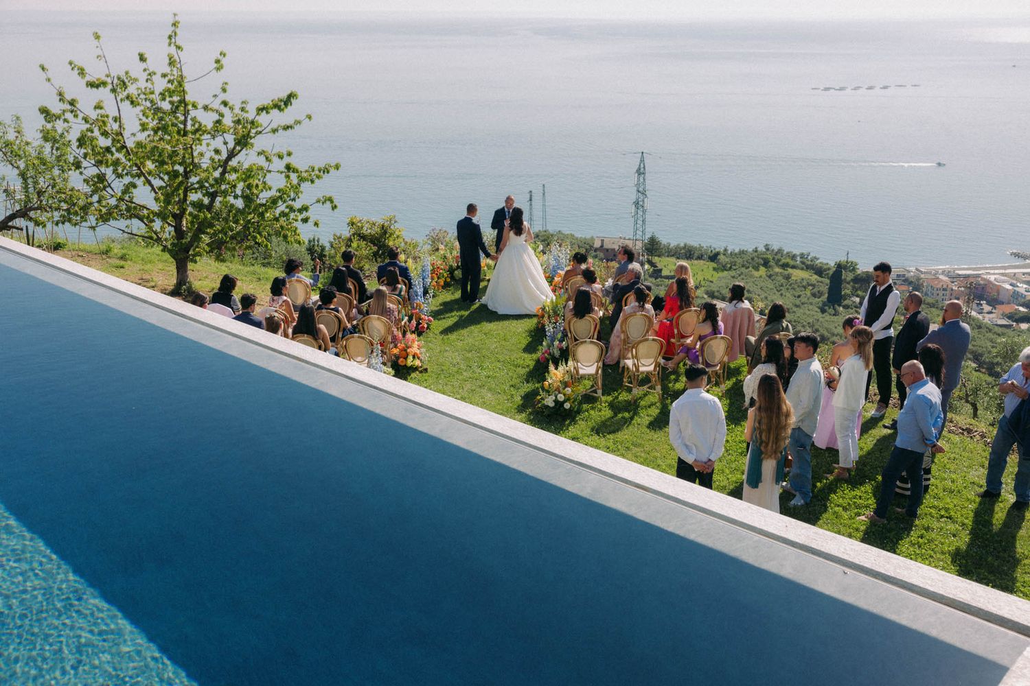 A panoramic collage of people gathering at an outdoor viewing area overlooking a coastal landscape on a sunny day.