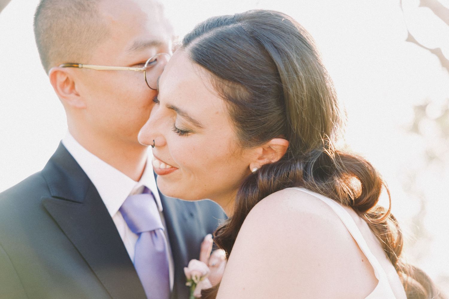 A romantic couple shares a tender kiss outdoors in soft natural lighting.