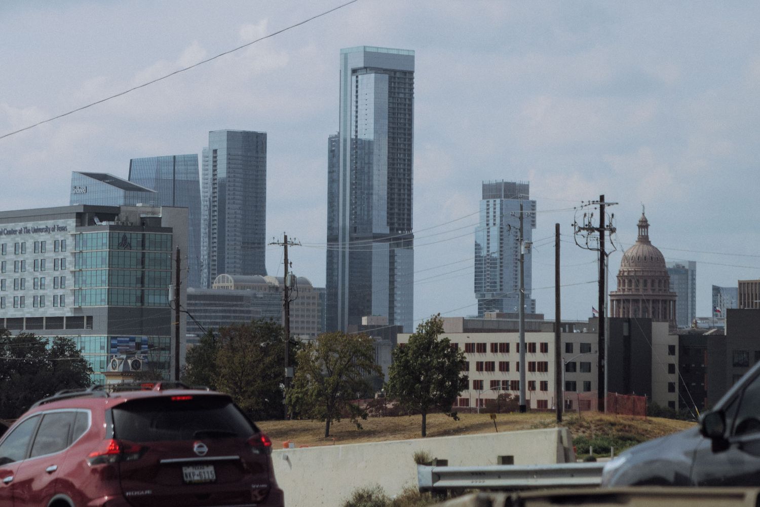Glass office towers and construction cranes dominate the downtown skyline against a cloudy sky.