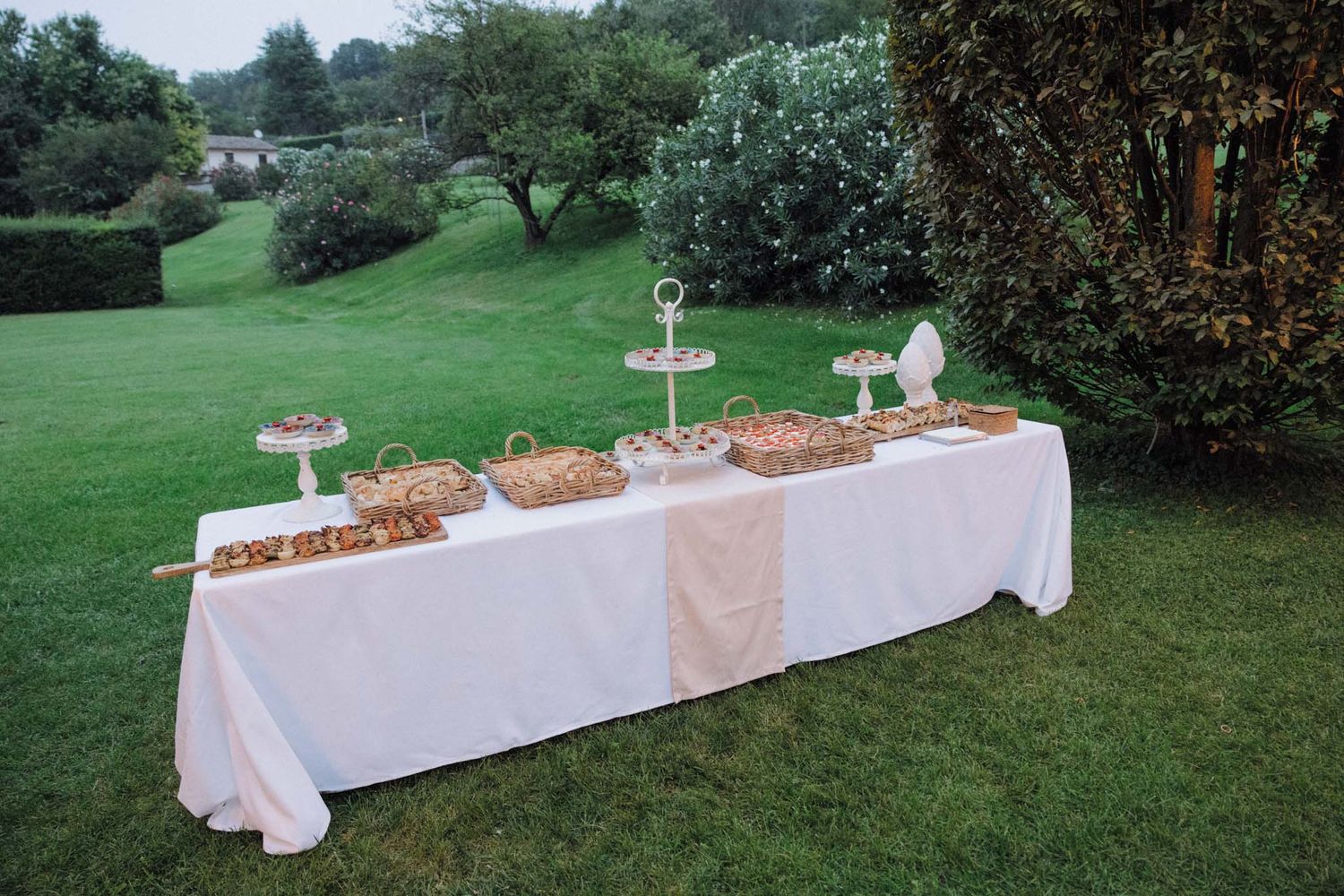White linen tablecloths with appetizers and food displays set up outdoors for an elegant garden party reception.