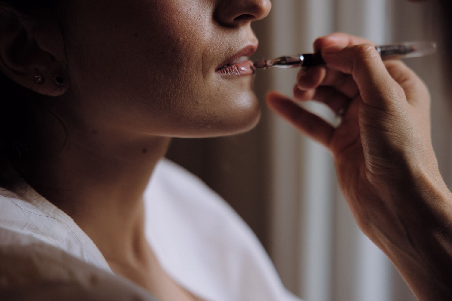 Close-up of someone applying lipstick with a makeup brush in a soft, warm lighting setting.