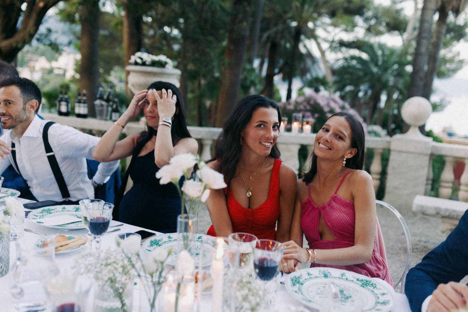 People gathered around an elegant outdoor dining table with white tablecloths and floral centerpieces at a social event.