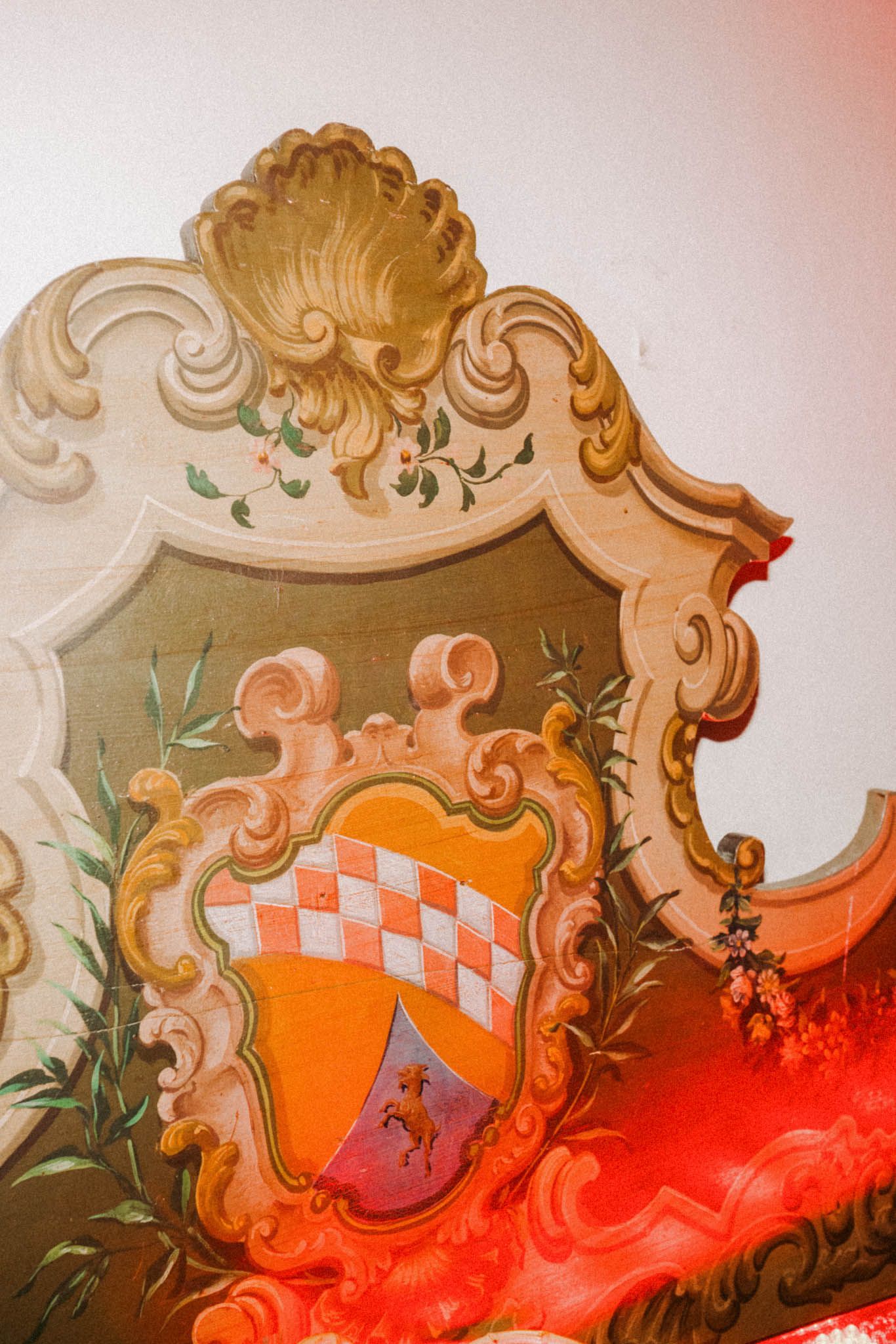 Ornate baroque-style architectural detail featuring scrollwork and decorative elements in orange and red tones against a light wall.