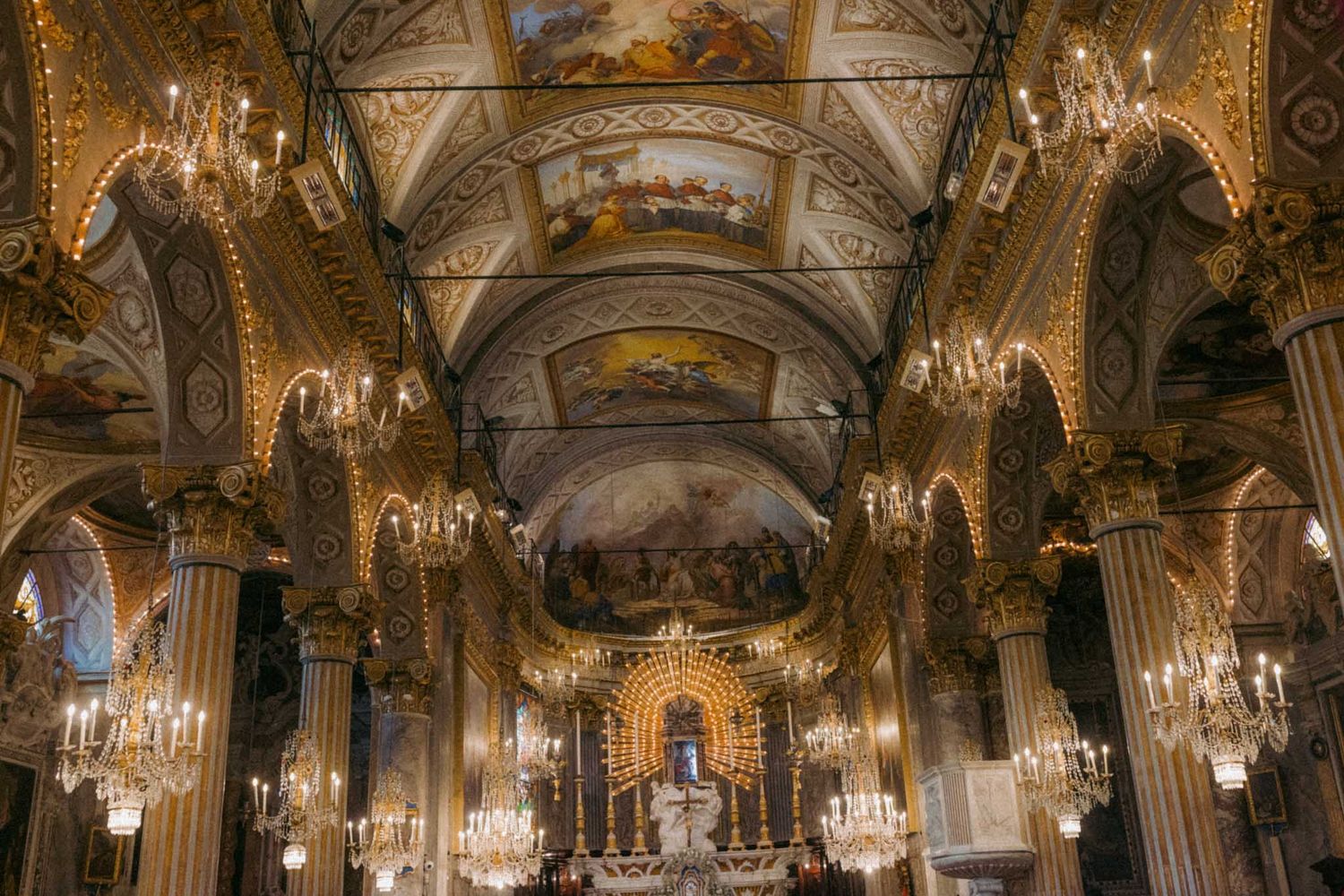 Ornate cathedral interior with vaulted ceiling, gilded arches, and crystal chandeliers illuminating the grand baroque altar.