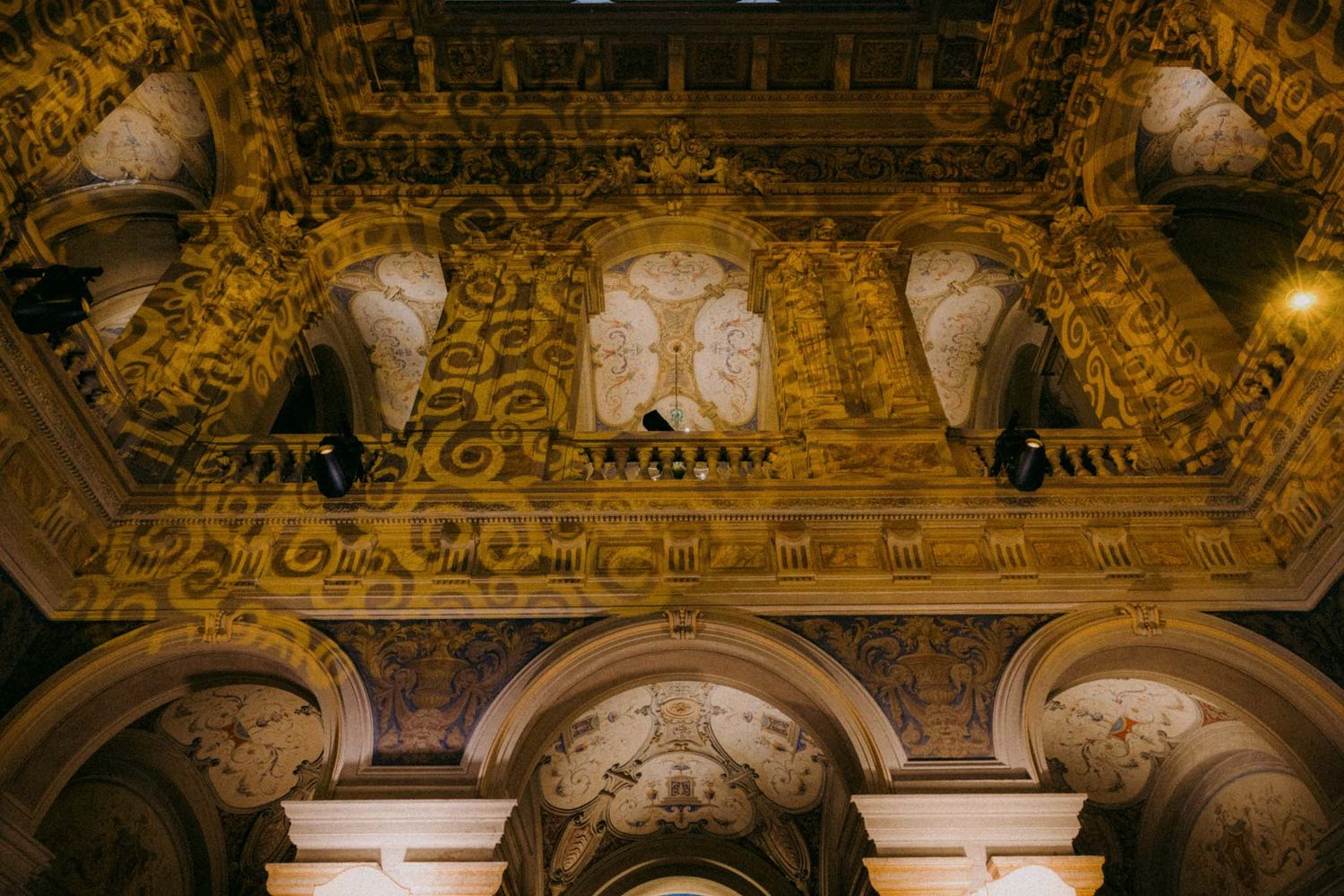 Ornate gold baroque ceiling with detailed frescoes and architectural details in a historic building.