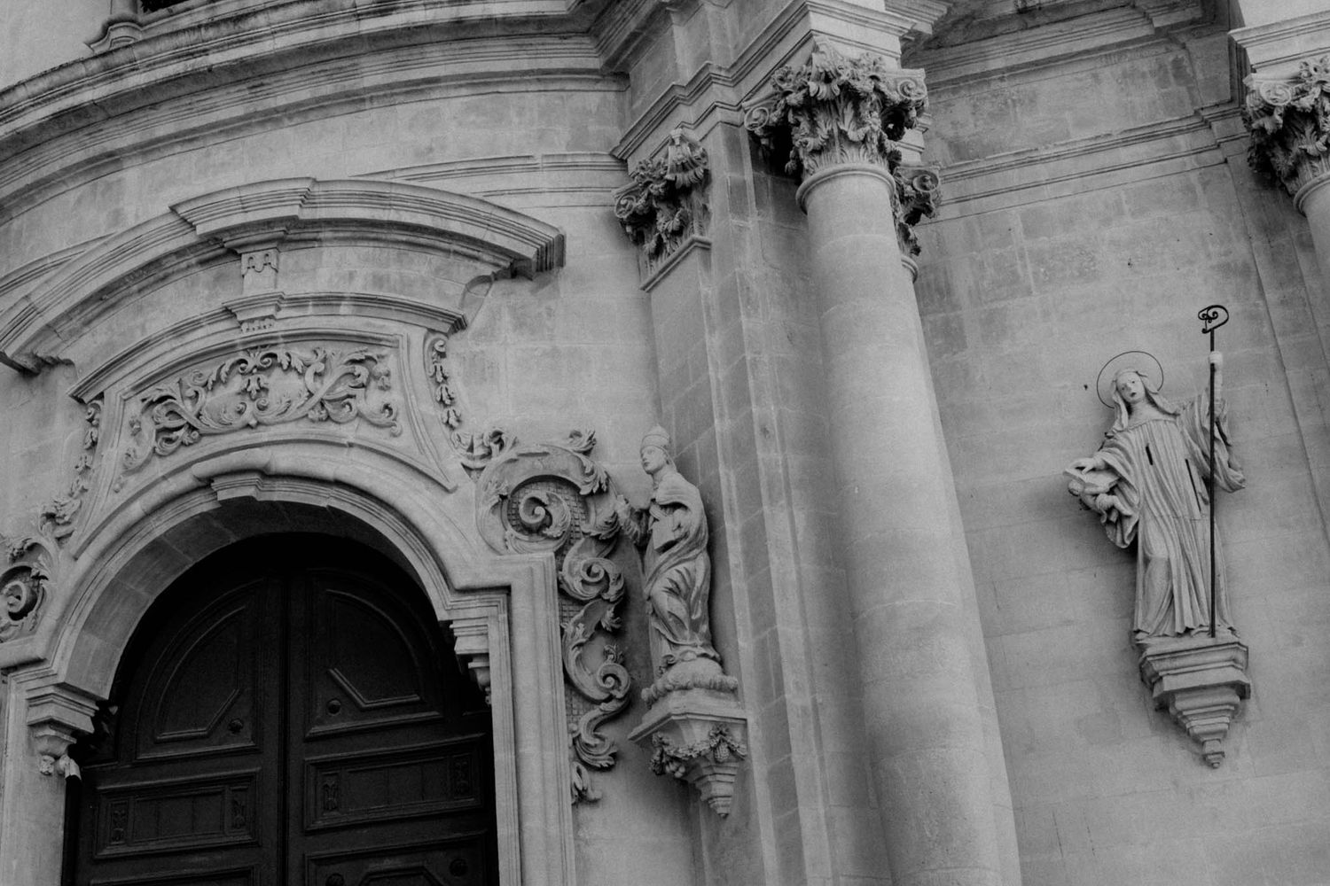 Ornate baroque church entrance with detailed stone carvings, columns and religious statues in black and white.