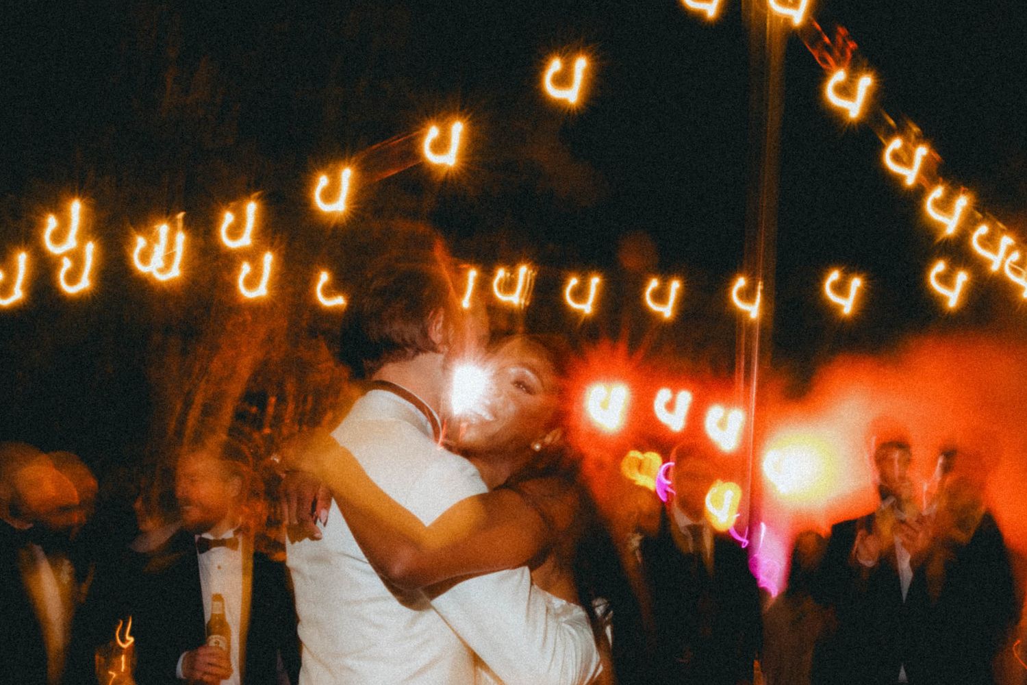 A couple dancing at an outdoor wedding reception under glowing string lights creating a romantic atmosphere.