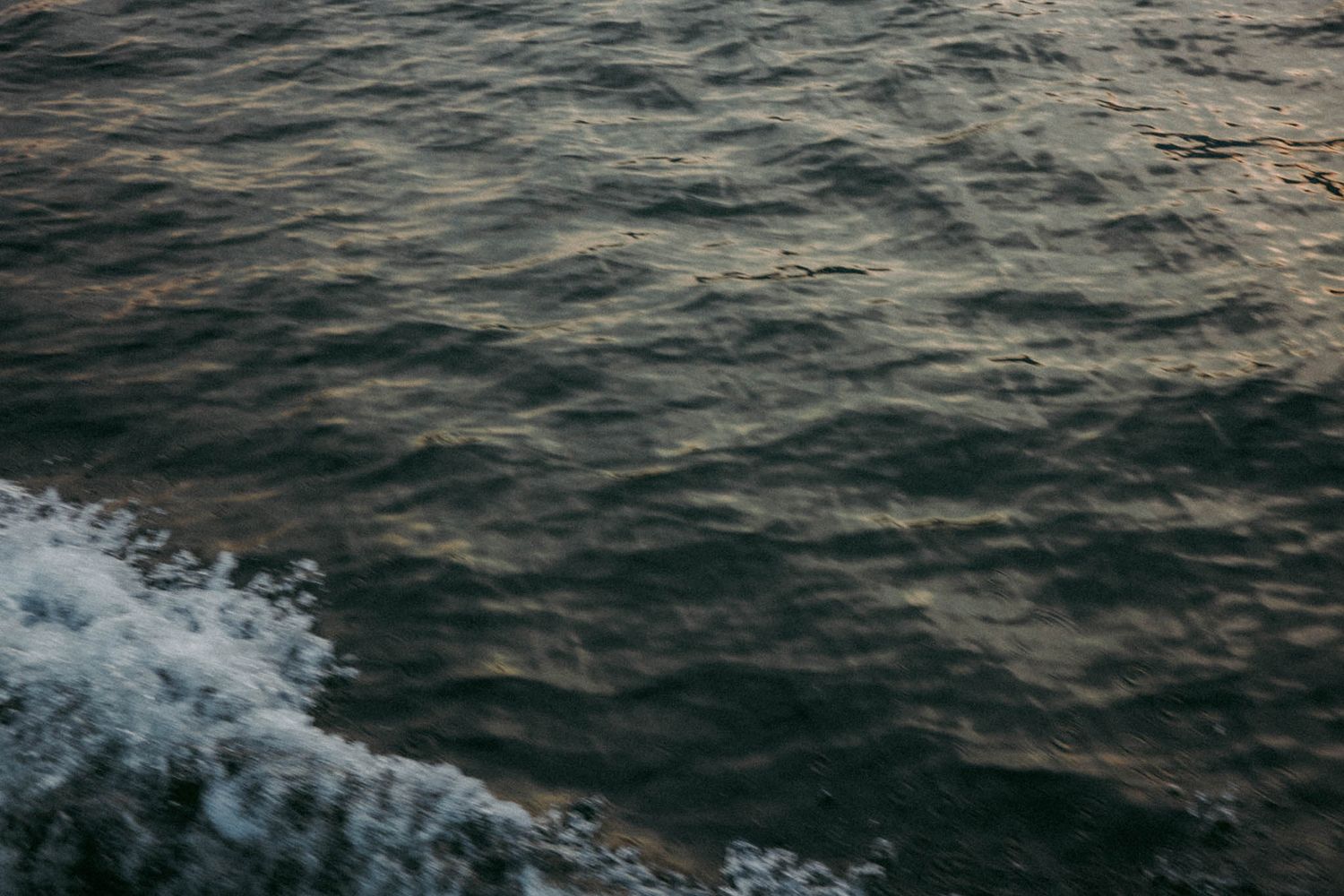 Aerial view of dark ocean waves crashing and creating white foam patterns on the water surface.