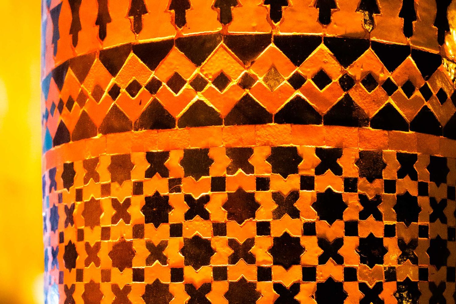 Orange and black patterned cylindrical lanterns create a geometric repeating design with warm glowing light.