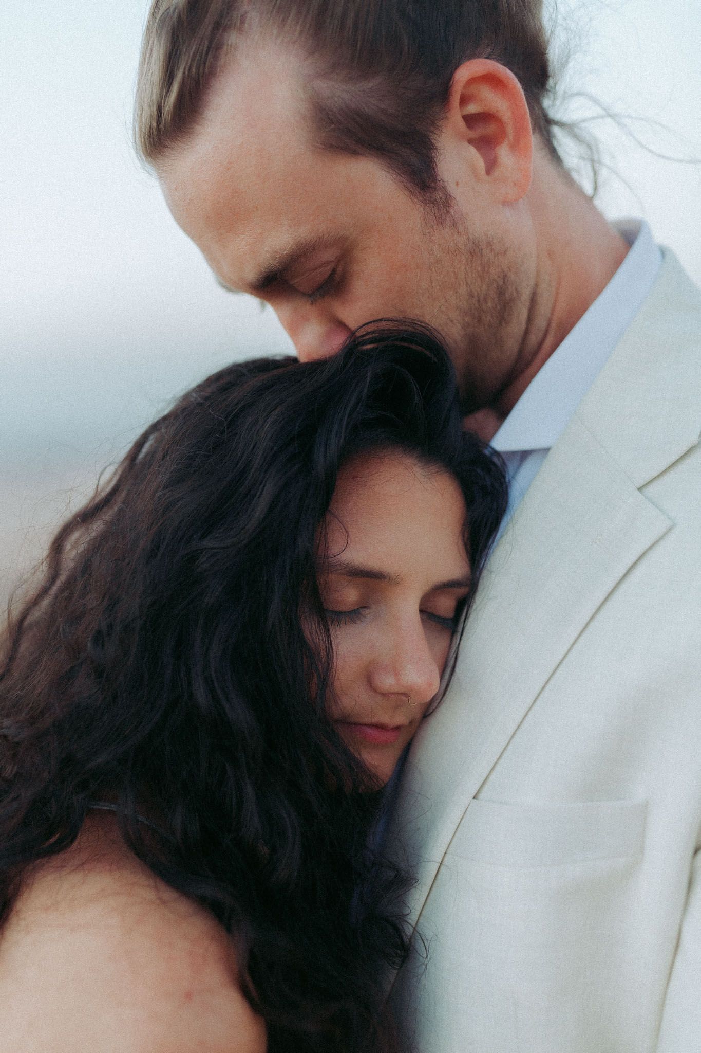 A romantic series of intimate portraits showing a couple in white clothing embracing against a light background.