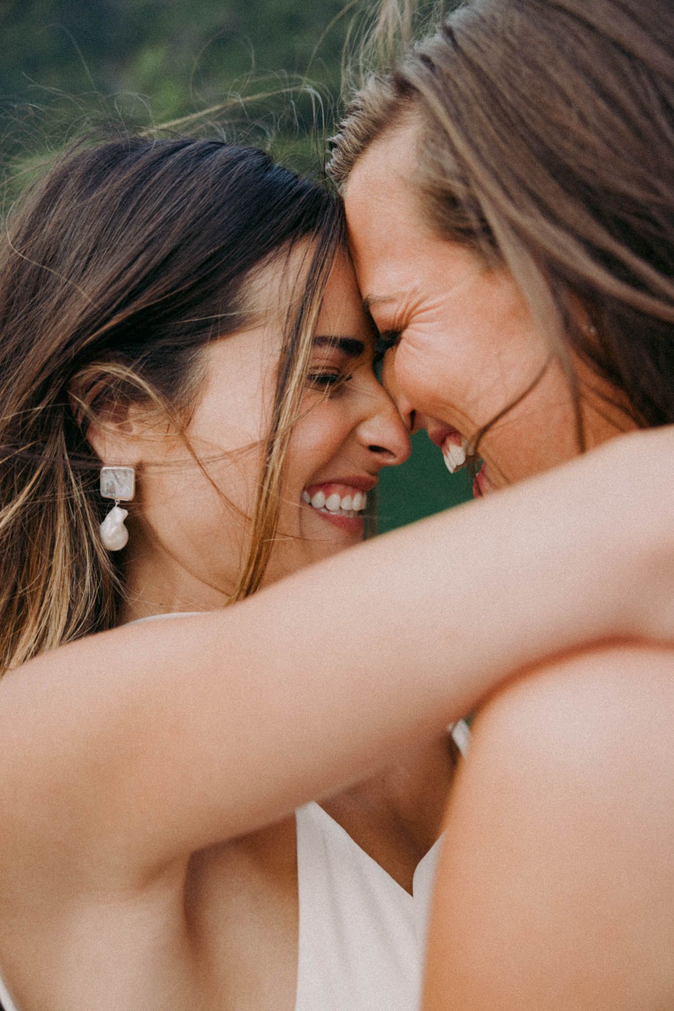 Close-up portrait of two people sharing an intimate moment outdoors with genuine smiles and foreheads touching.