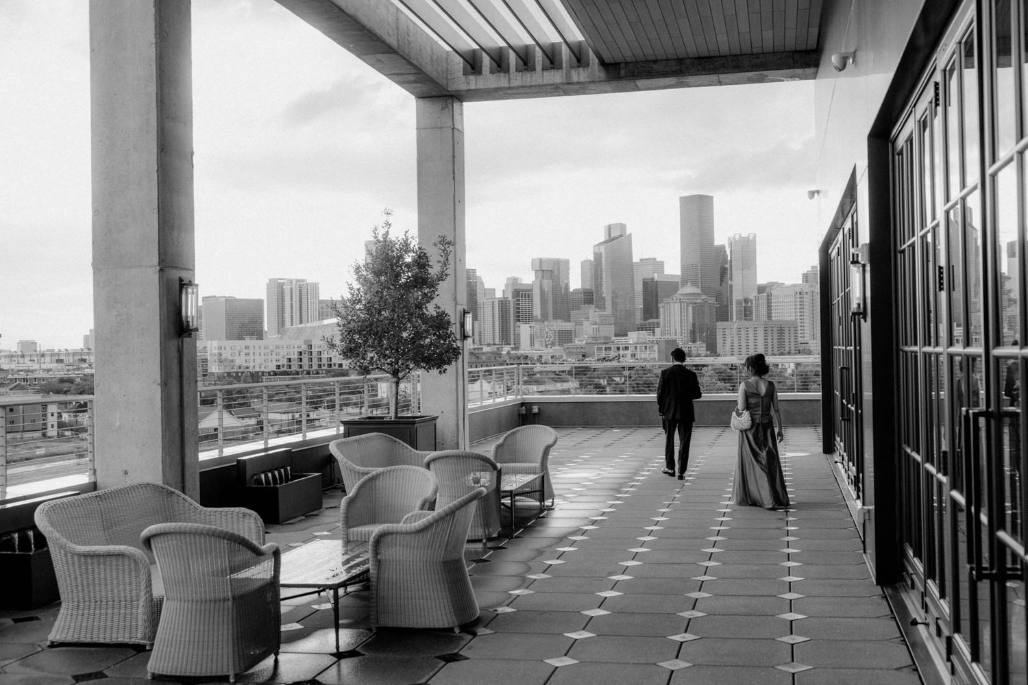 Modern rooftop lounge area with white chairs and city views through glass panels on a cloudy day.