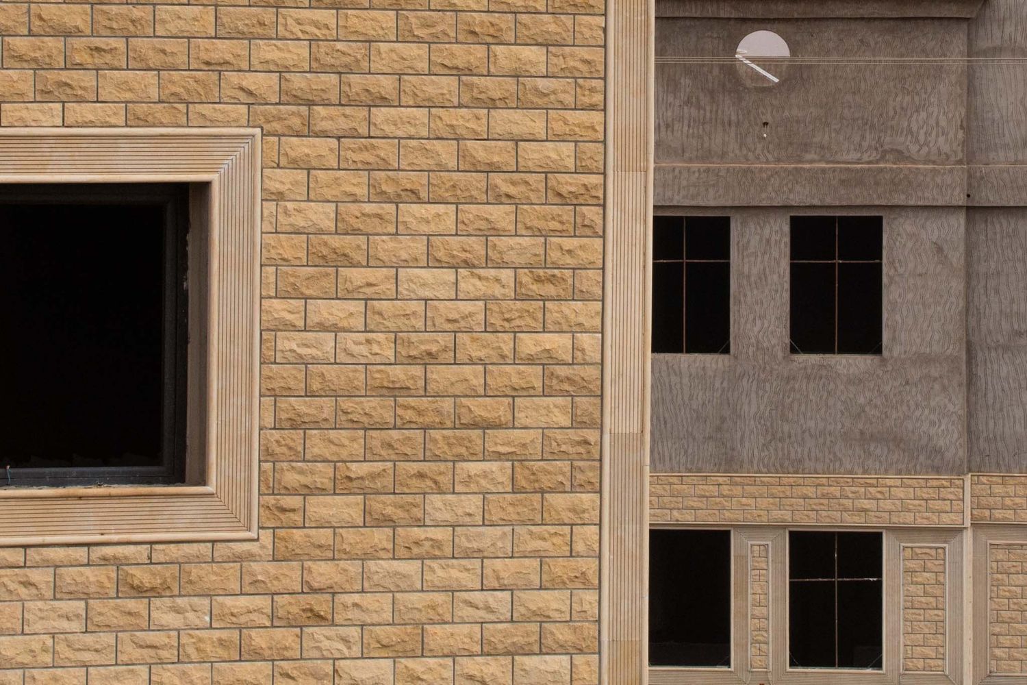 Exterior wall of a building featuring tan brick facade with square windows and concrete accents.