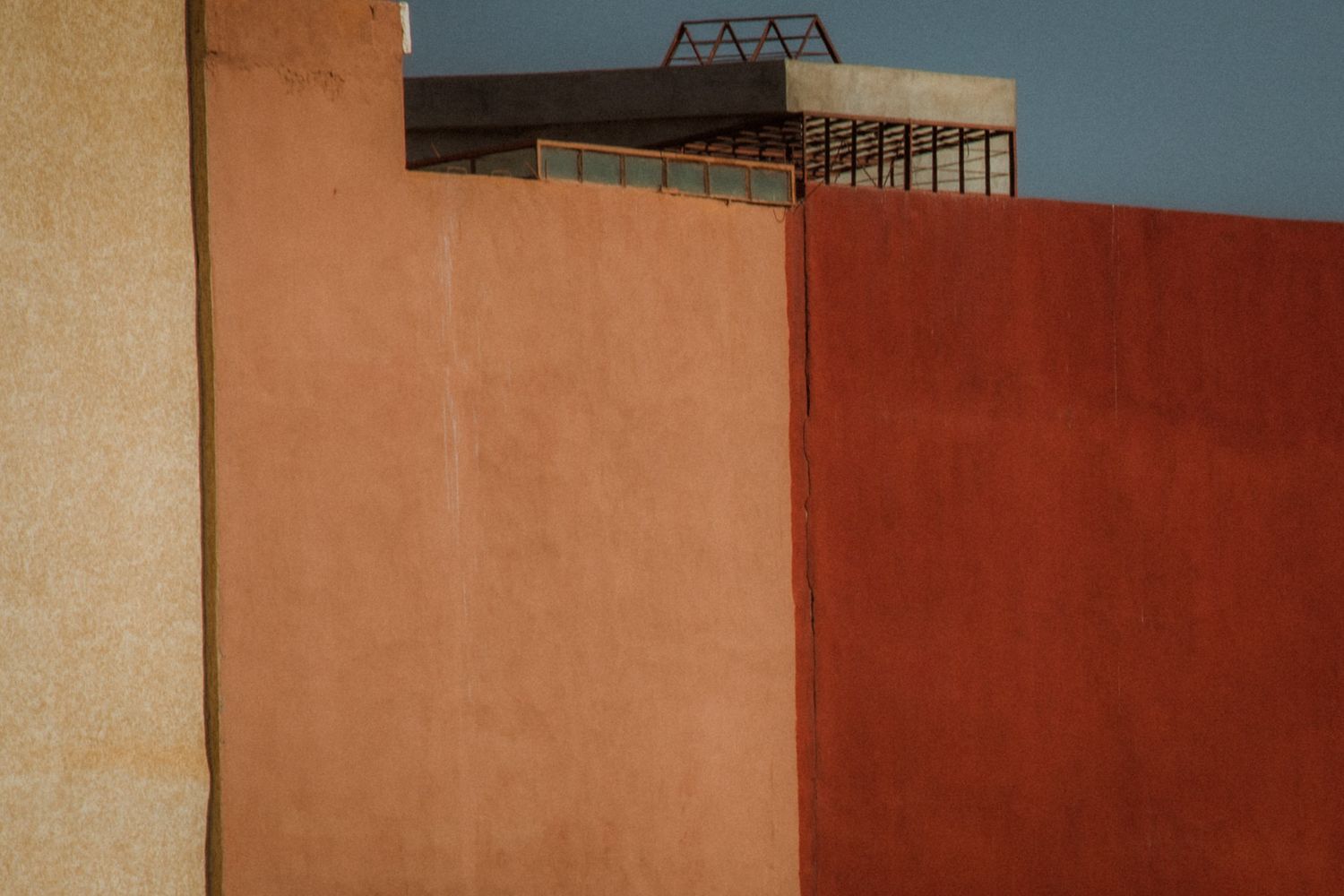 Minimalist urban architecture featuring orange and beige walls under a blue sky with geometric shapes.