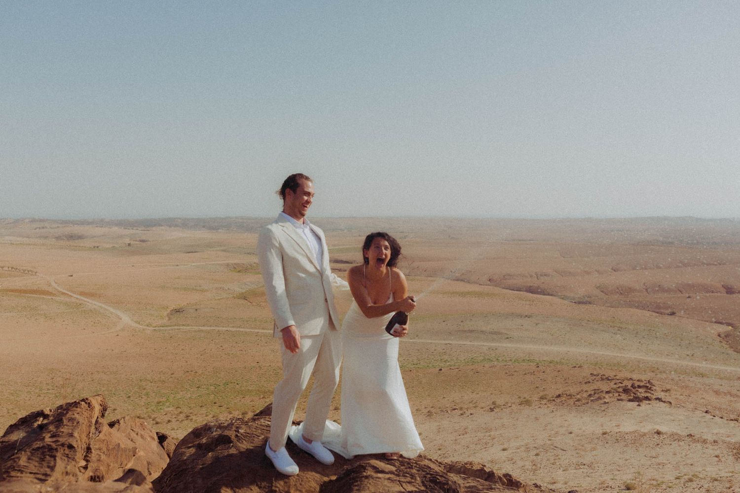 People walk through a vast desert landscape with rolling sand dunes stretching to the horizon.