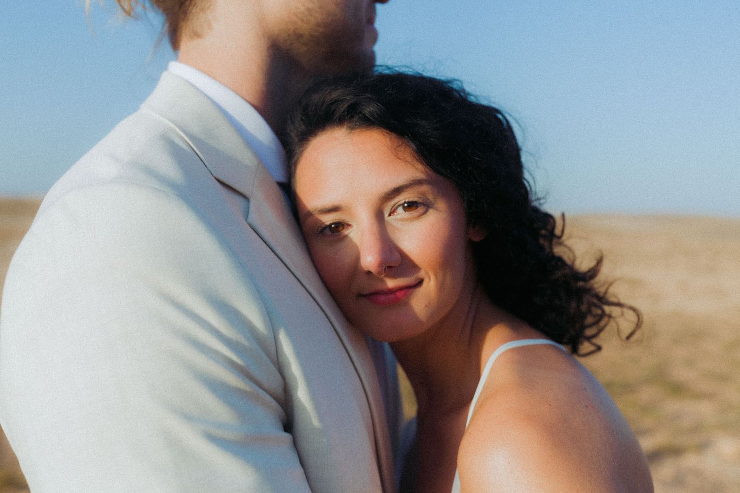 Romantic desert engagement photoshoot with couple embracing against sandy backdrop at sunset.