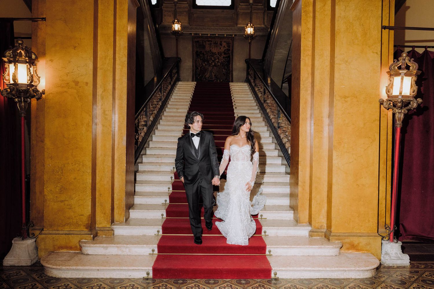 A grand staircase with yellow walls and red carpet leads upward in an elegant interior setting.