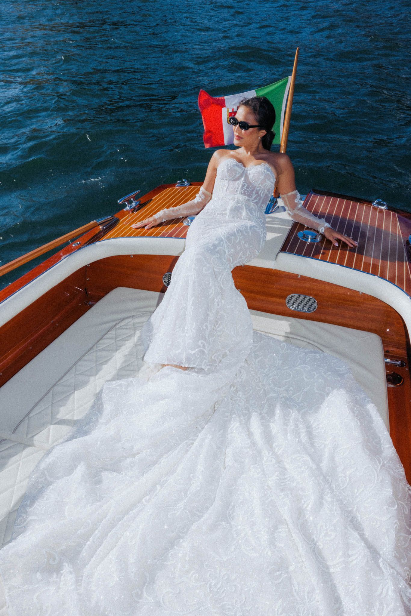 A white wedding dress with a full tulle skirt elegantly draped across a classic wooden boat deck on the water.