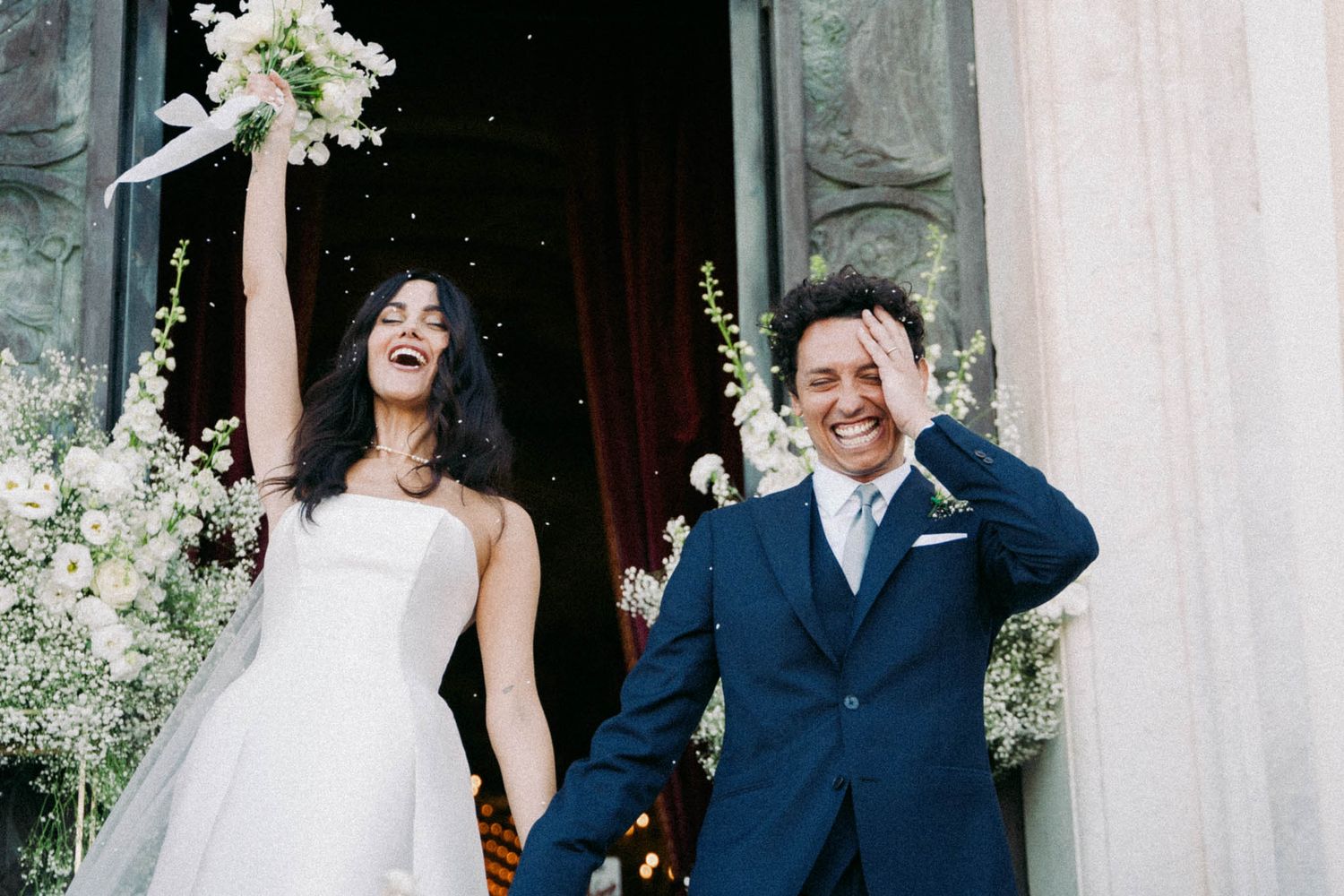 A joyful couple shares a candid moment during their wedding celebration outdoors by white columns.