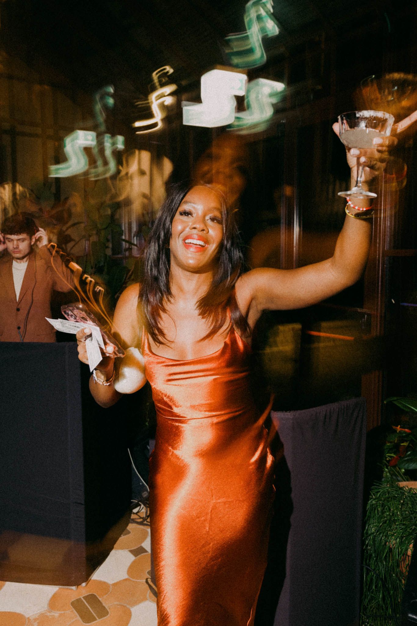 Person in a shimmering orange dress dances joyfully at a nighttime event, captured in a sequence of motion shots.