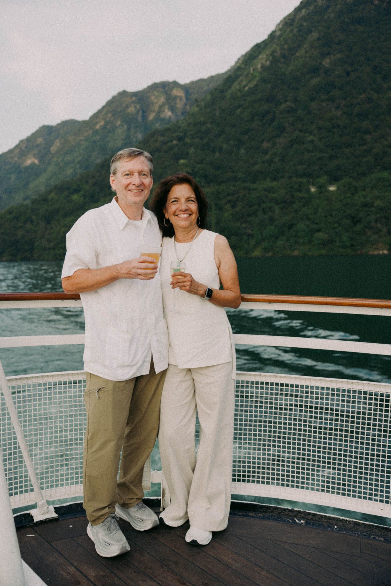 Couple enjoying a romantic moment on a cruise ship deck with scenic mountain views across the water.