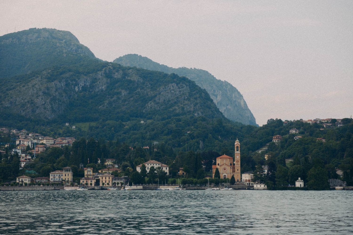 Panoramic view of Lake Como's mountainous shoreline with historic buildings nestled along the waterfront in Italy.