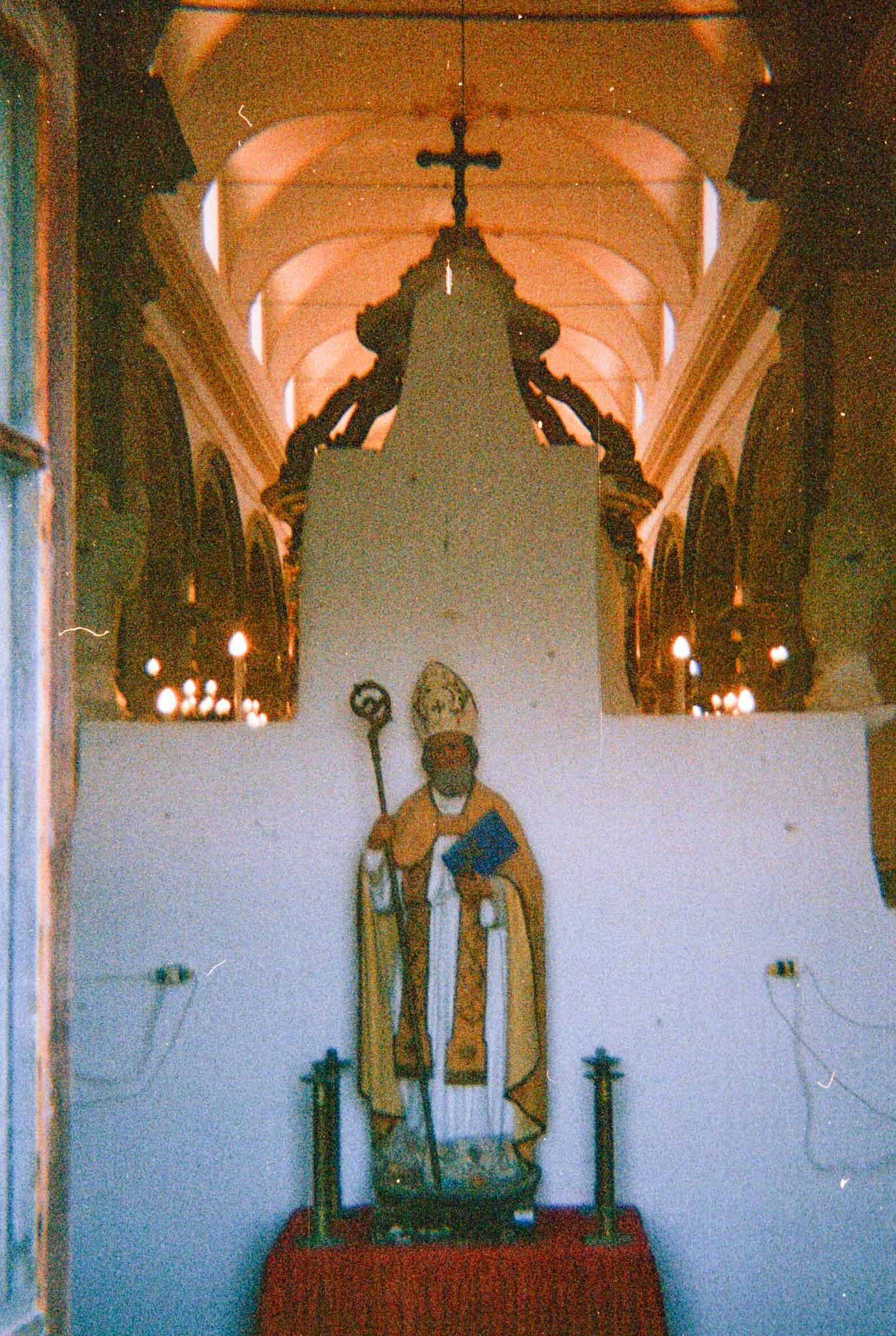 Gothic church interior with vaulted ceilings and religious statues illuminated by warm lighting.